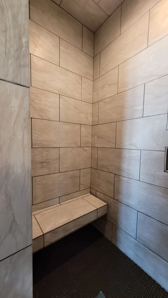 Beige ceramic tiled shower with built-in seating bench and dark mosaic floor