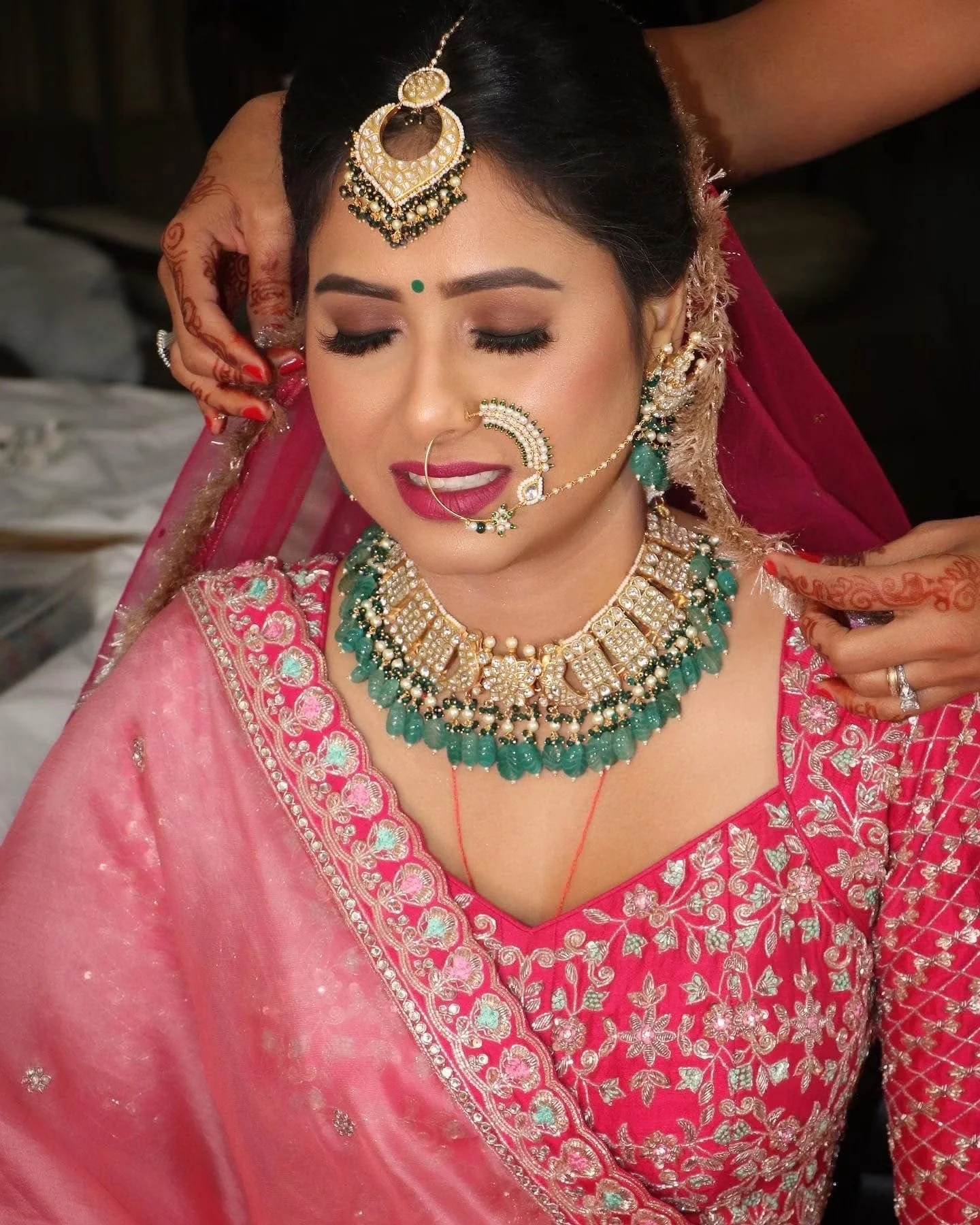 A woman dressed in traditional Indian attire with intricate jewelry and henna on her hands, having her hair styled.