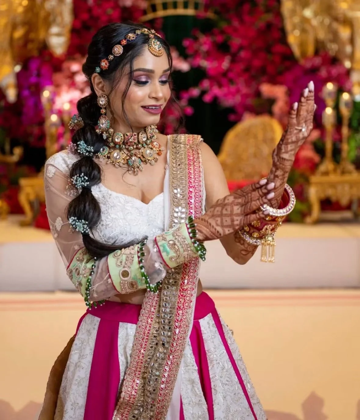 A woman dressed in traditional Indian wedding attire with mehndi designs on her hands, jewelry, and a decorated background with flowers.