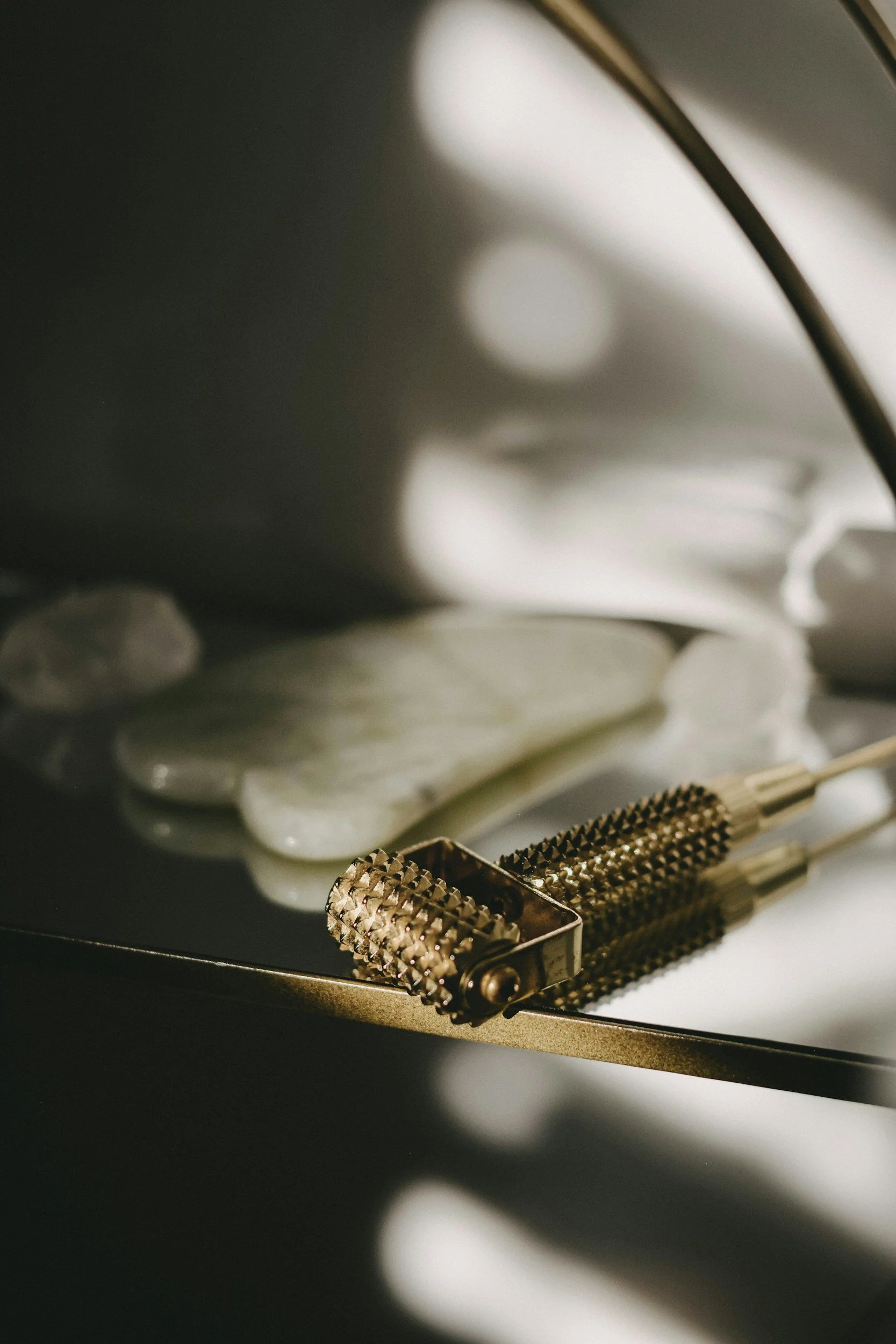 Close-up of a vintage safety razor with textured metal handle resting on a reflective surface, with blurred round light reflections in the background.
