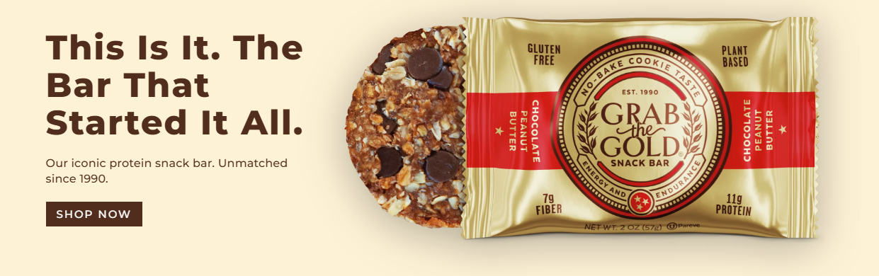 A protein snack bar called 'Grab the Gold' with a partially unwrapped caramel-colored packaging showing the flavor 'Chocolate Peanut Butter' and a bitten section revealing the inside with chocolate chips and nuts. The text emphasizes it as an iconic, high-protein, gluten-free, plant-based snack with 7g fiber and 11g protein, established in 1990.