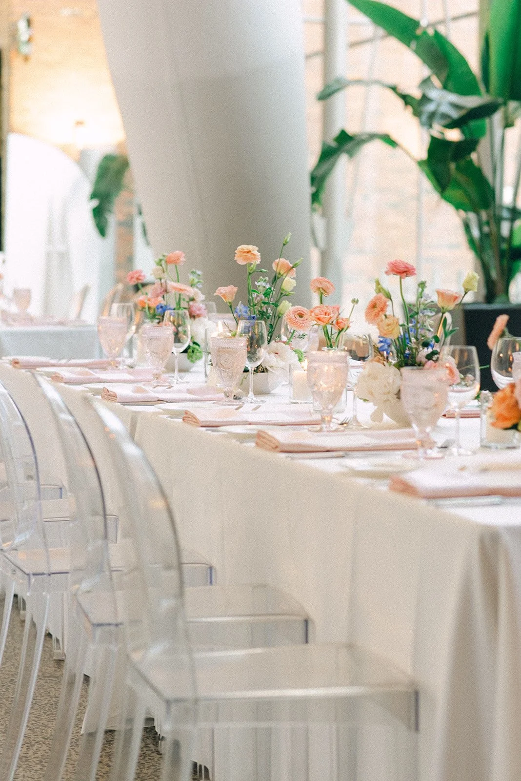 Elegant table setting with floral centerpieces, glassware, and pink napkins, in a decorated indoor venue.