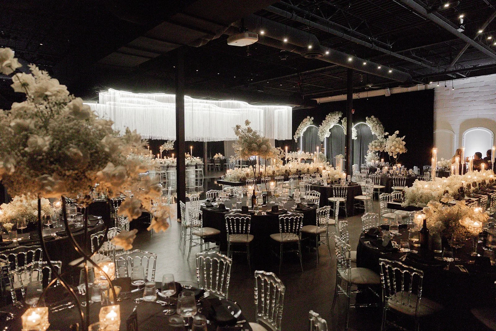 Elegant event space decorated with lavish white floral arrangements, candlelit tables, and modern lighting fixtures for a formal celebration or wedding reception.