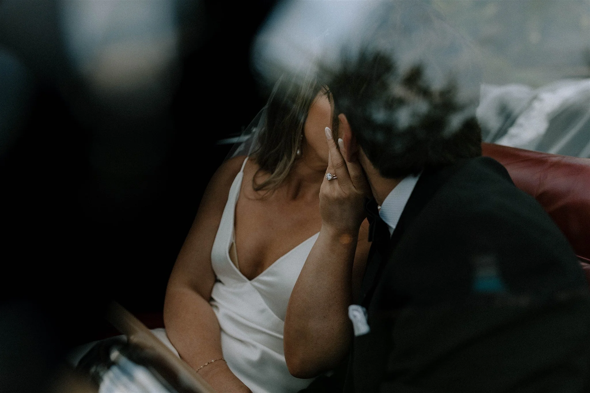 A couple sharing a kiss at a wedding ceremony, with the woman wearing a white dress and a ring on her finger.