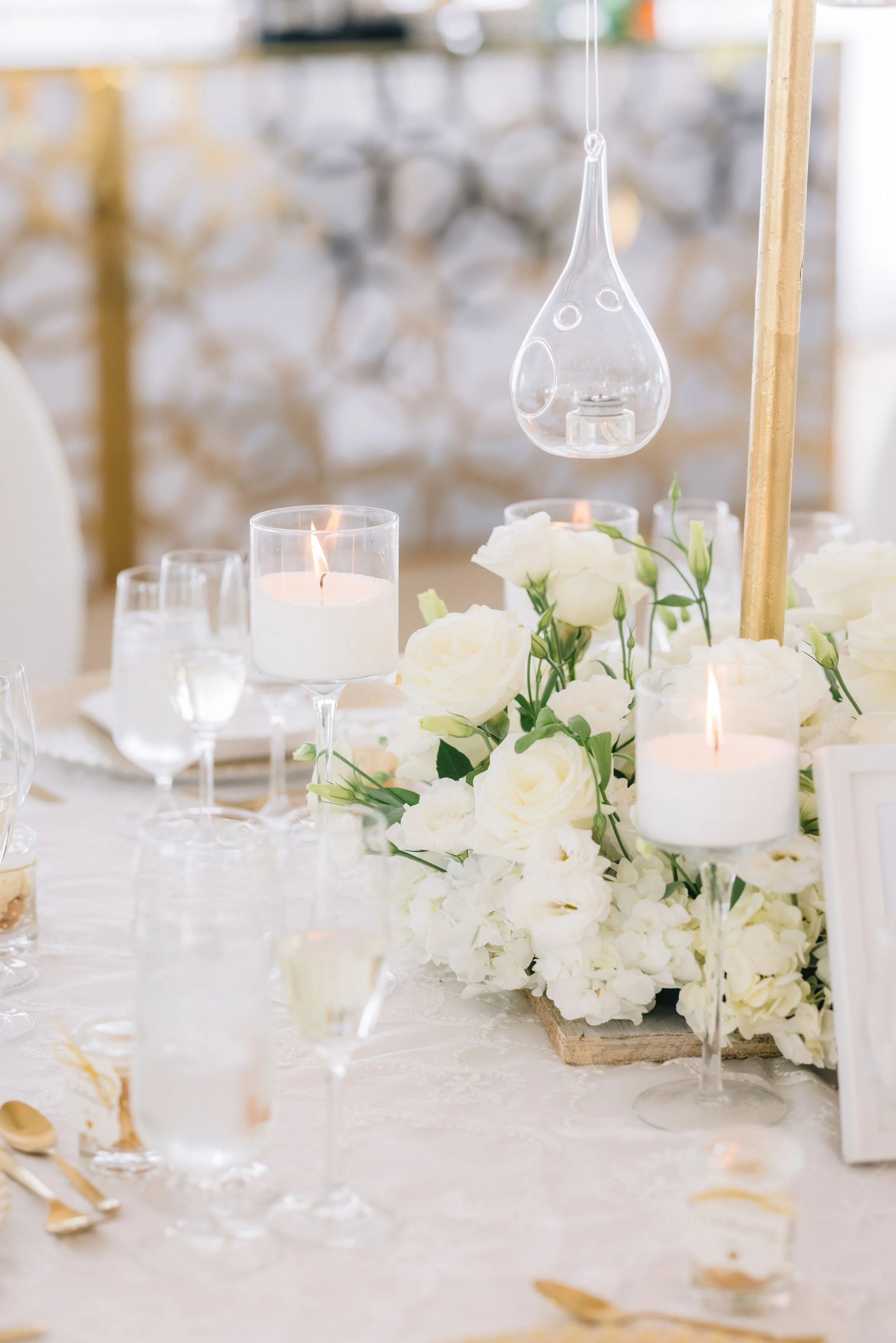 Elegant table setting with white roses, candles, and glassware, decorated for a wedding or formal event.