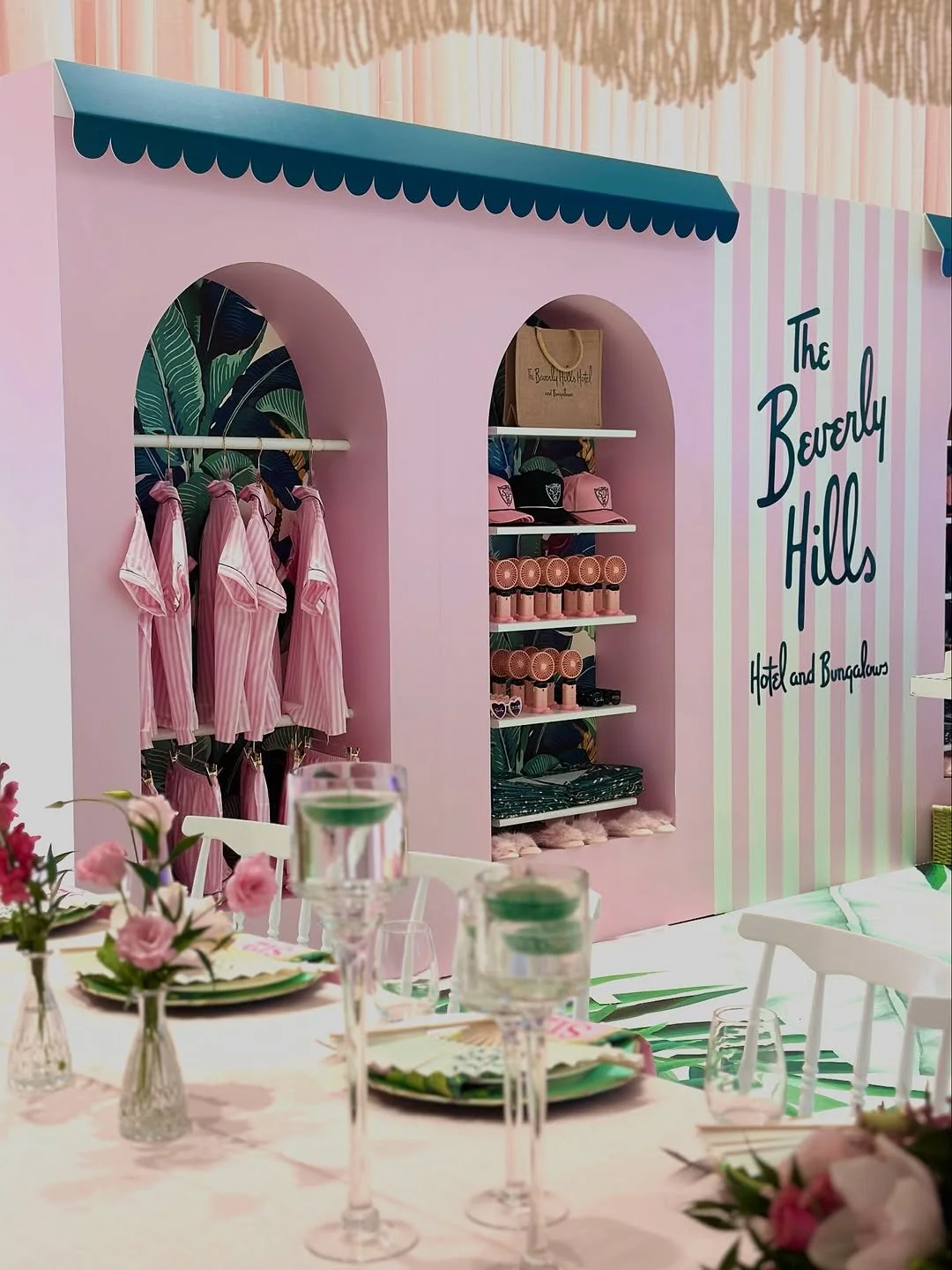 Decorative display with pink and white striped walls, showcasing pink striped pajamas, caps, and rolled towels at The Beverly Hills Hotel and Bungalows, with table settings and floral arrangements in the foreground.
