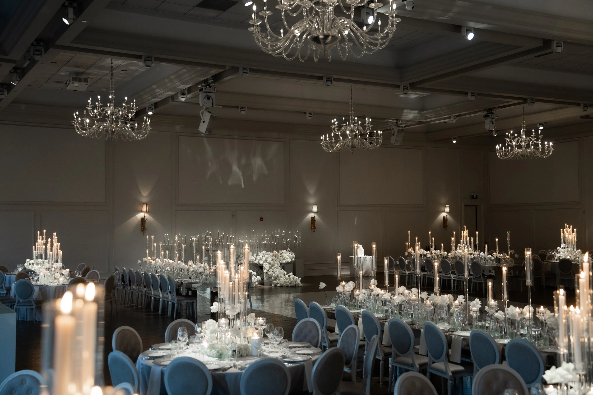 Elegant banquet hall decorated for a formal event with chandeliers, candles, and floral centerpieces.