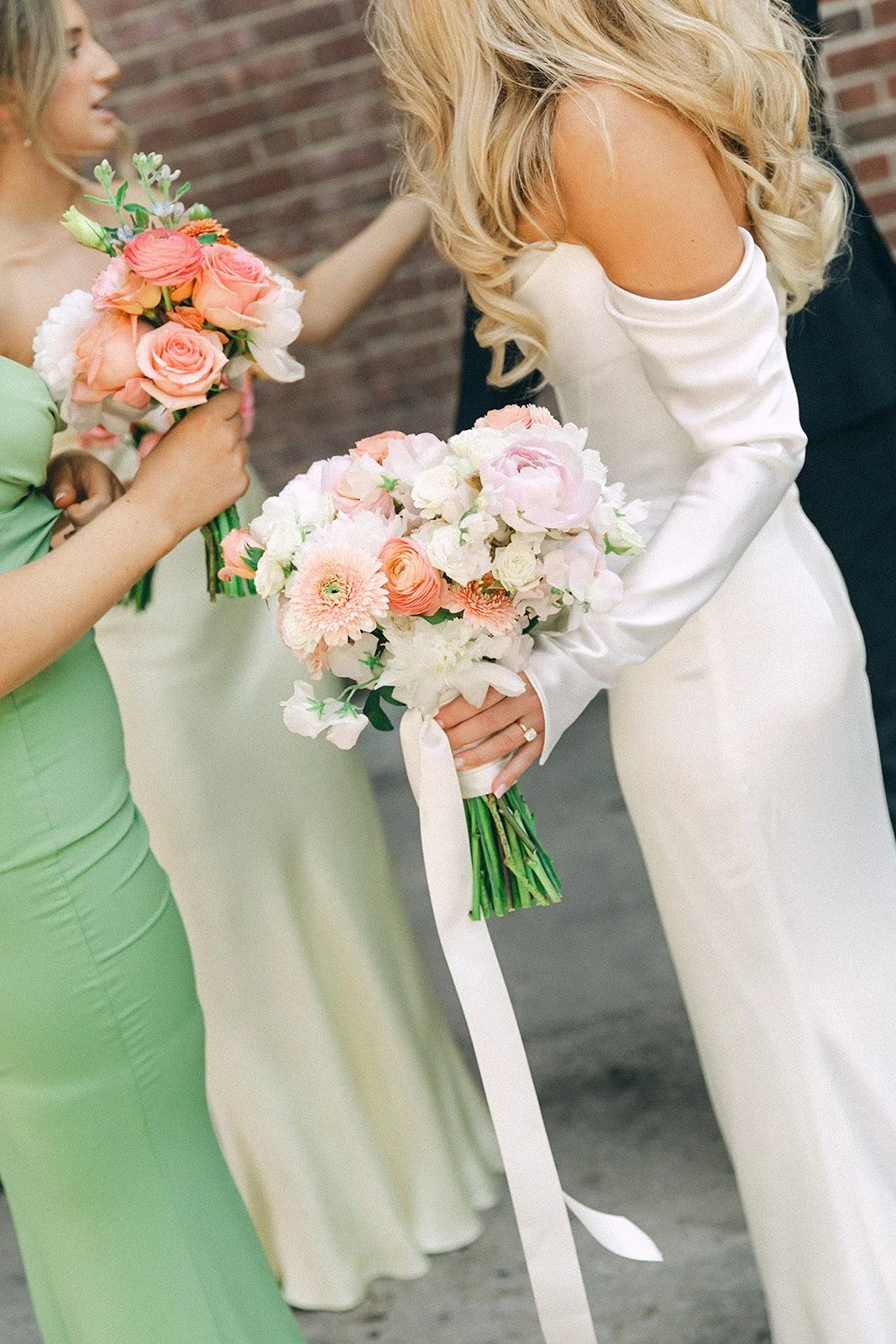 A bride in a white dress holding a bouquet of pink and white flowers at a wedding, with a woman in a green dress holding a similar bouquet nearby.