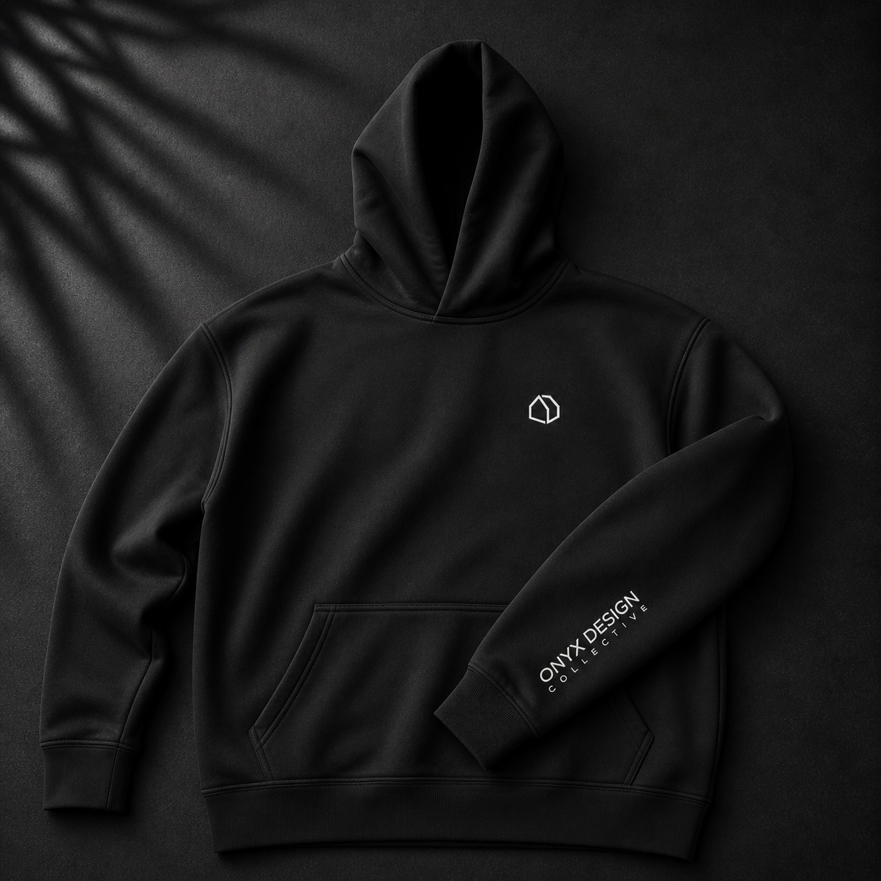Black hoodie with a small geometric logo on the chest and the text 'ONYX DESIGN COLLECTIVE' on the sleeve, placed on a dark background with shadows.