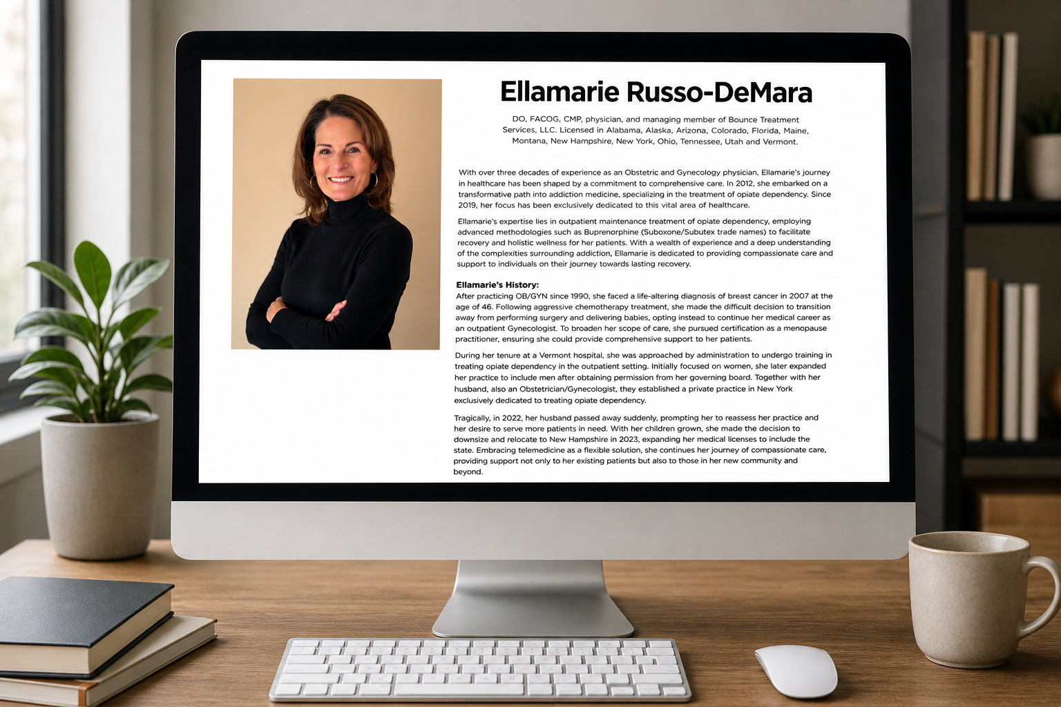 Computer monitor displaying a professional biography of Ellamarie Russo-DeMara with her photo, alongside potted plant, coffee mug, keyboard, and mouse on a wooden desk.