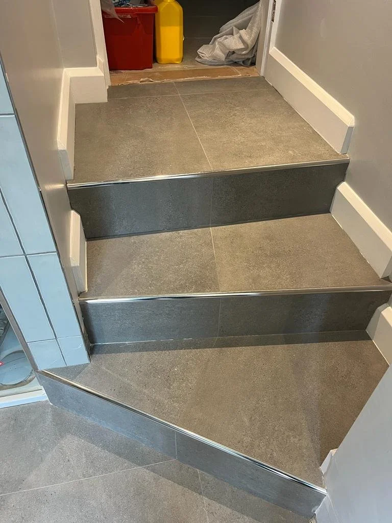 Three-step stone staircase leading up to a doorway, with a tiled floor in the foreground and cleaning supplies in the background.