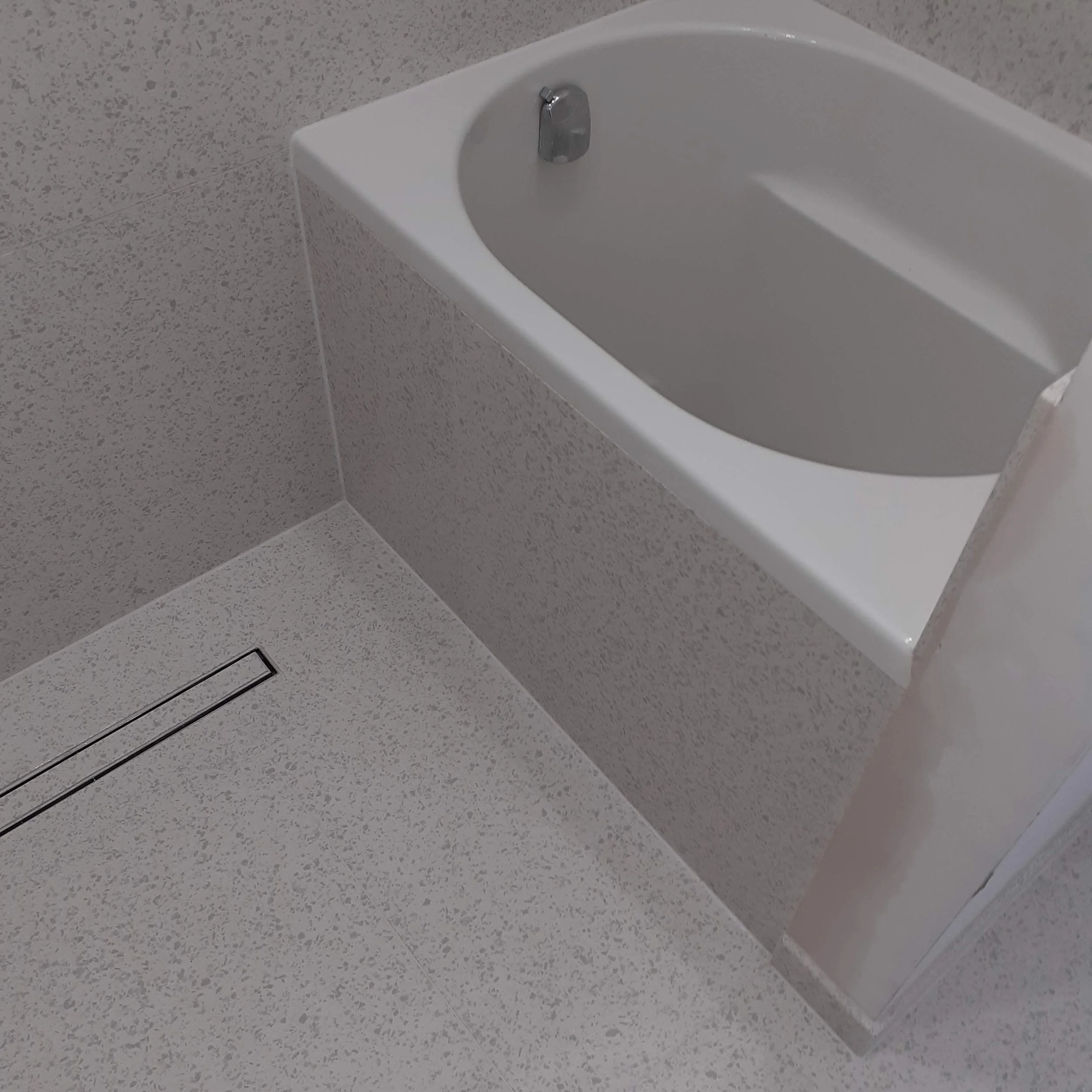 Gray speckled tiled walls and floor, and a drain on the floor nearby.