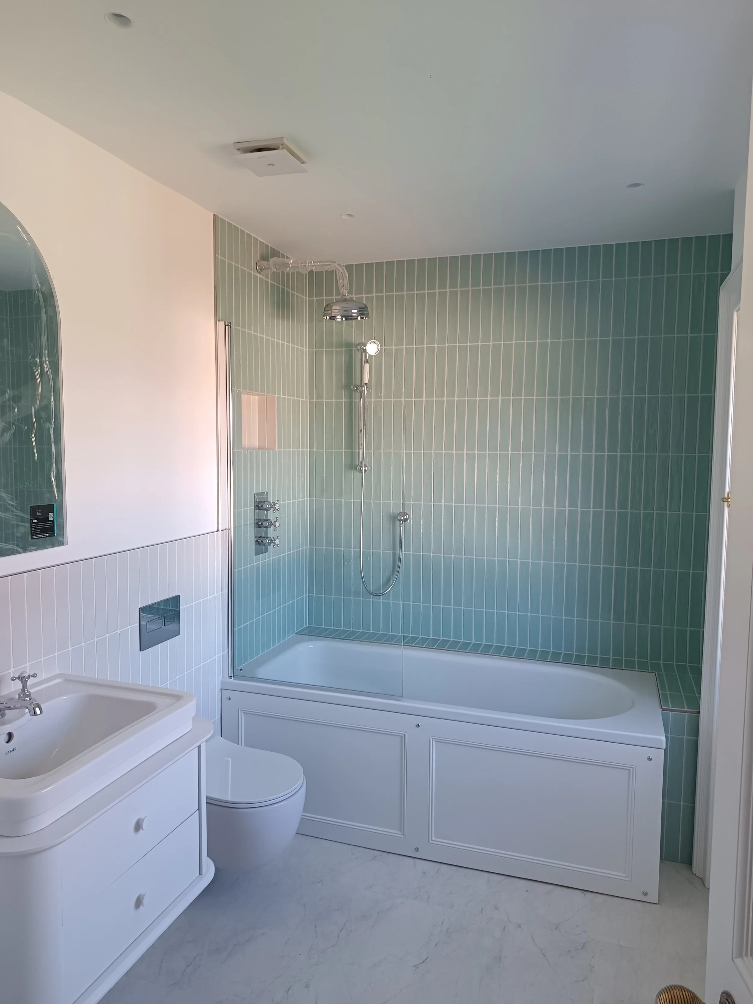 Bathroom with green tiled shower area, a white bathtub, a white sink vanity, and a mirror.
