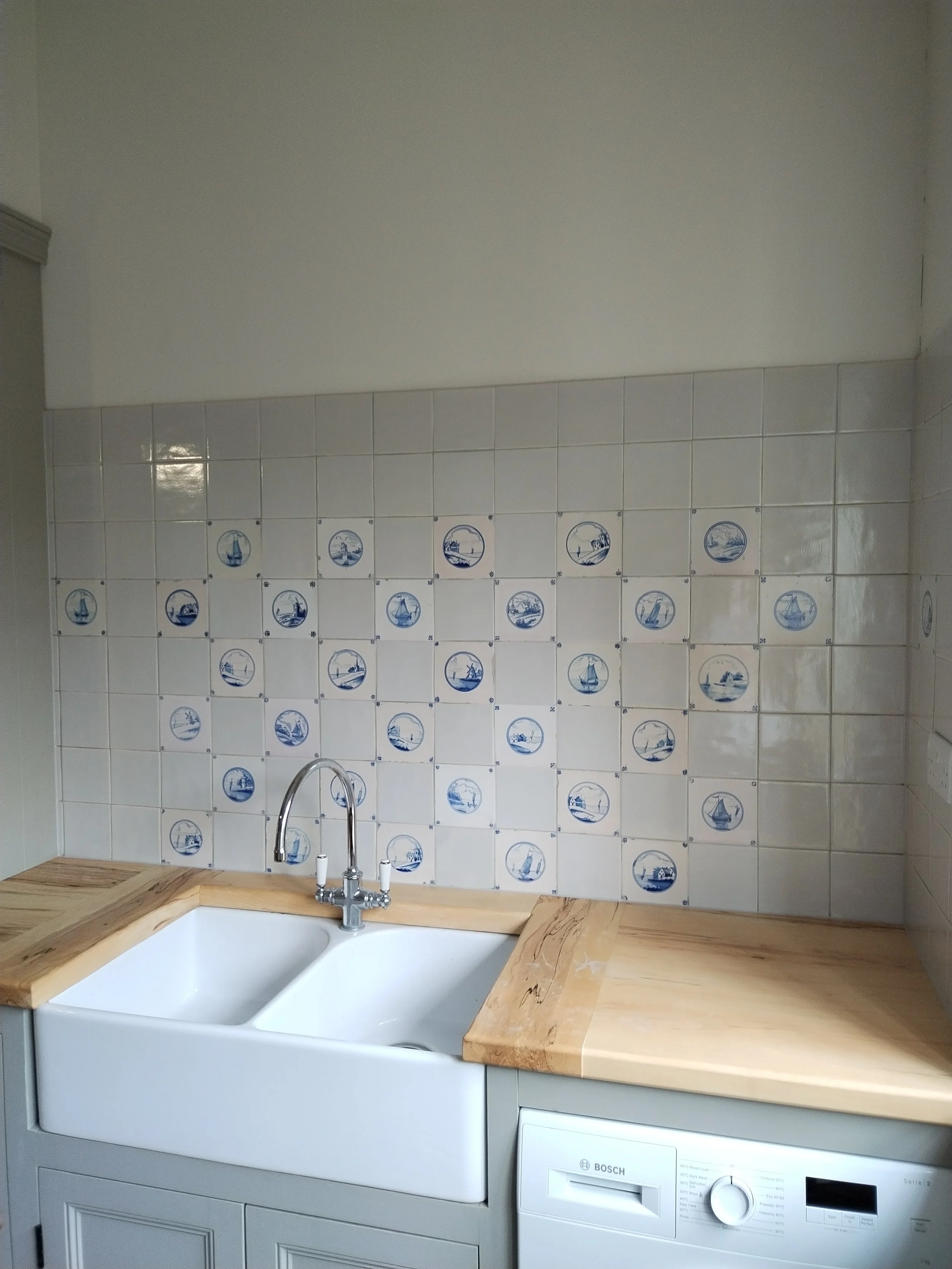 Kitchen with a white farmhouse sink, wooden countertop, tiled wall with nautical-themed blue and white tiles, and a washing machine beneath the counter.