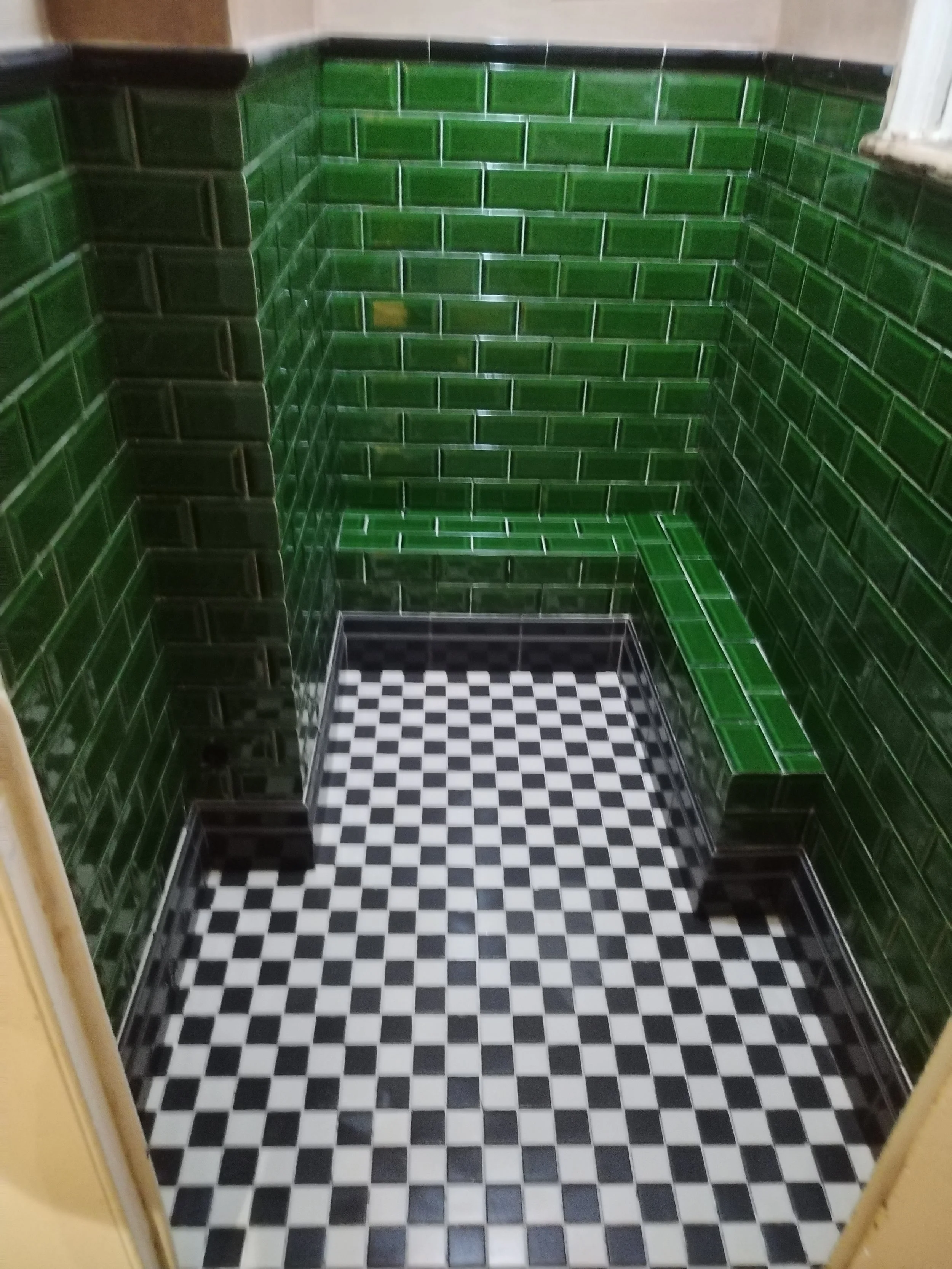 A small corner space with green tiled walls and a black and white checkered tile floor.