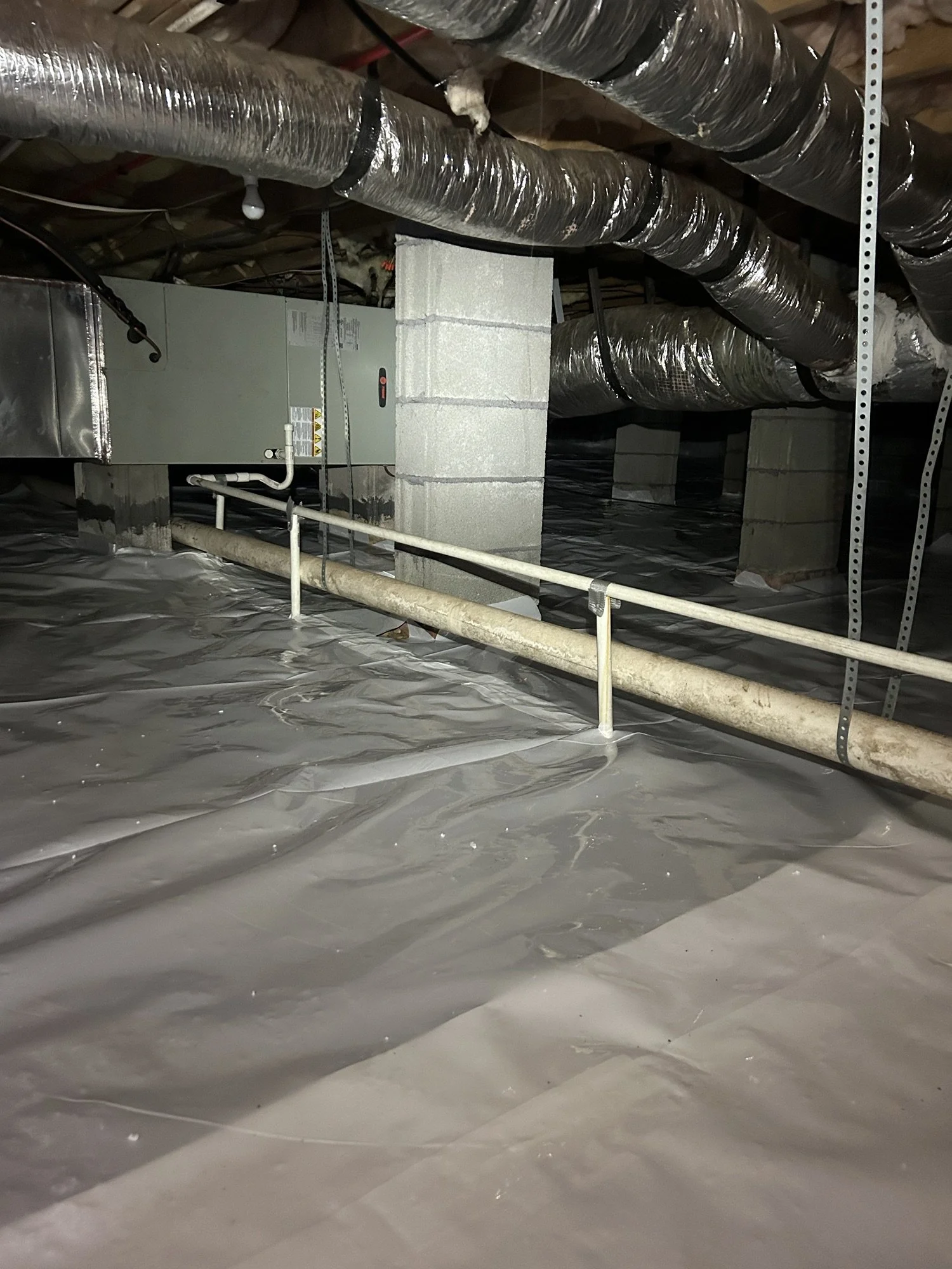 Basement with ductwork, concrete block support columns, pipes, metal beams, and a floor covered with plastic sheeting.
