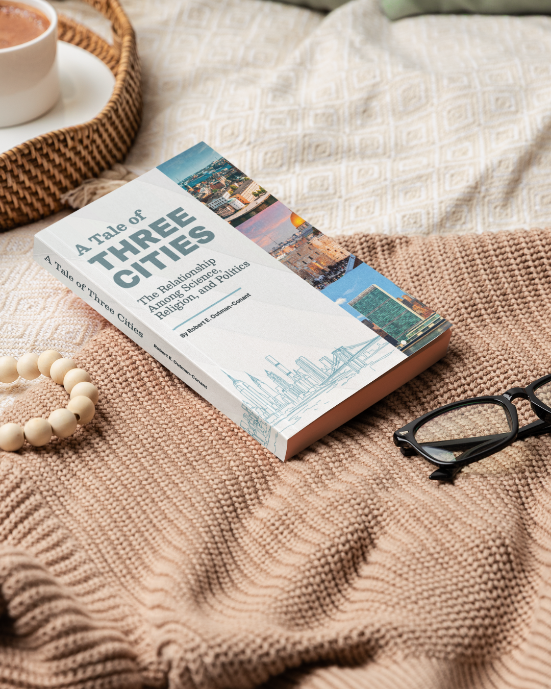 A book titled "A Tale of Three Cities" on a textured bedspread, with a pair of black reading glasses nearby, and a cup of coffee on a tray in the background.