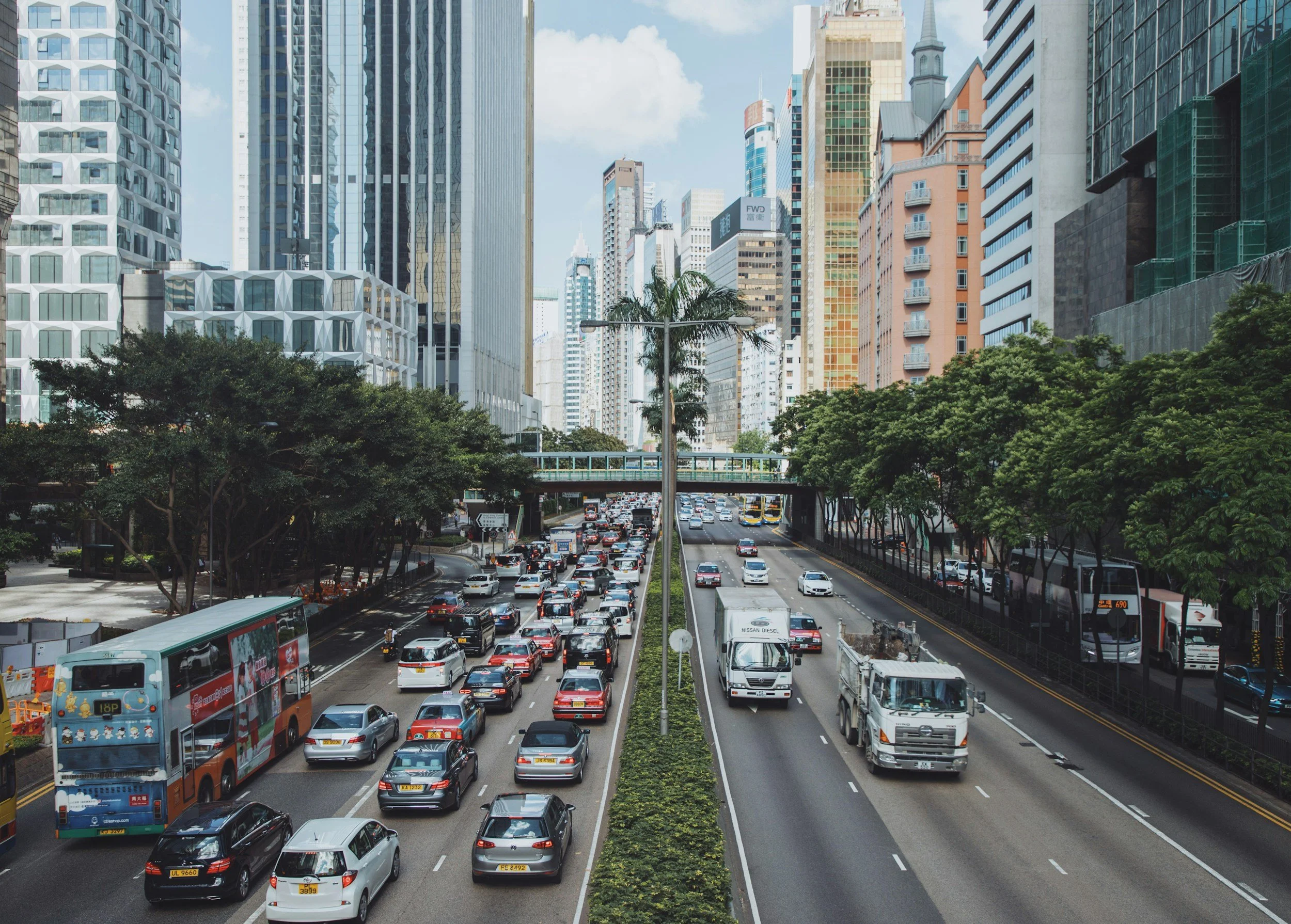A highway divided by a grassy median and palm trees with  buildings on either side of the road.