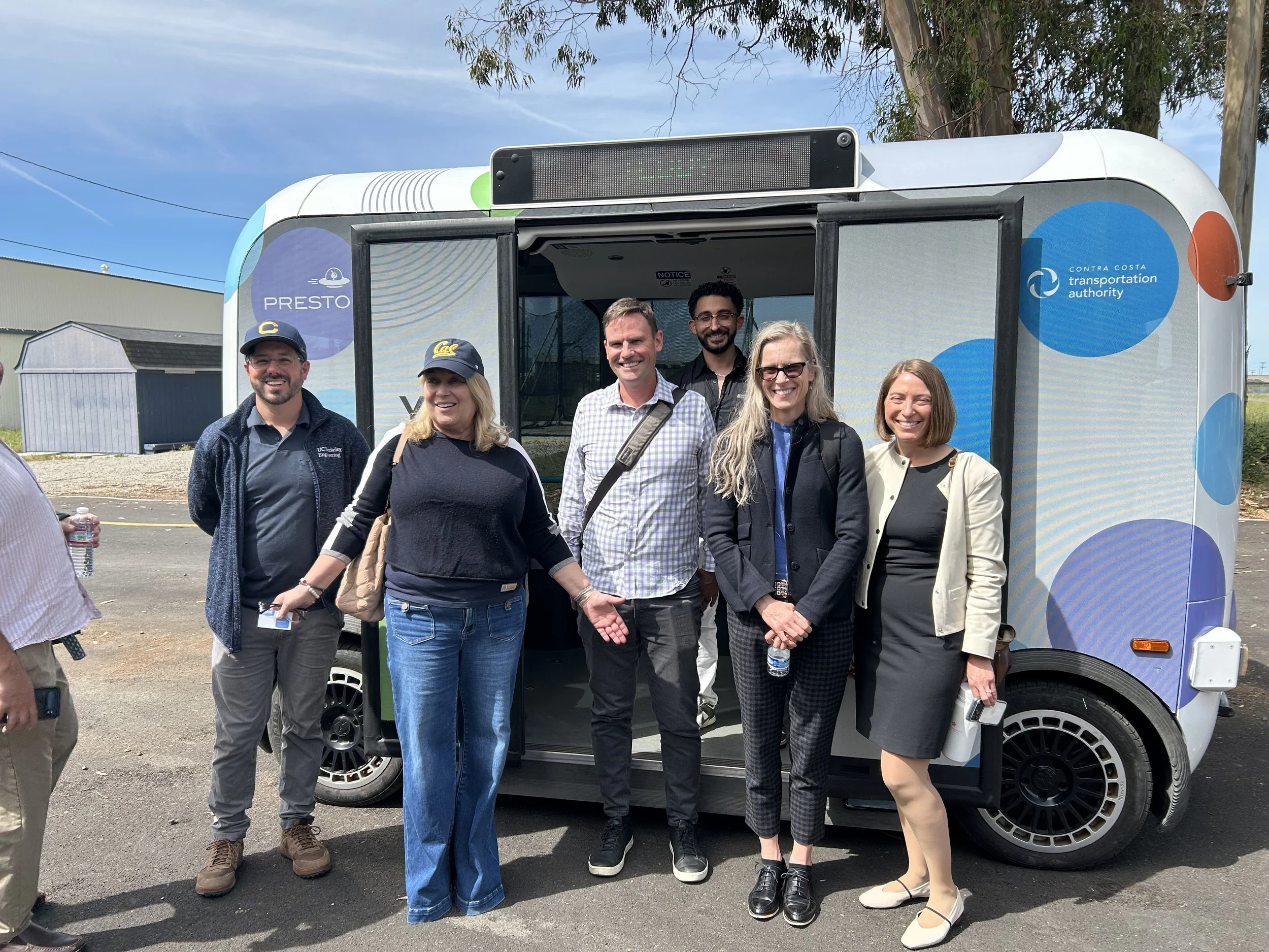 Seval Oz with her arms spread with a group of people in front of an autonomous vehicle.