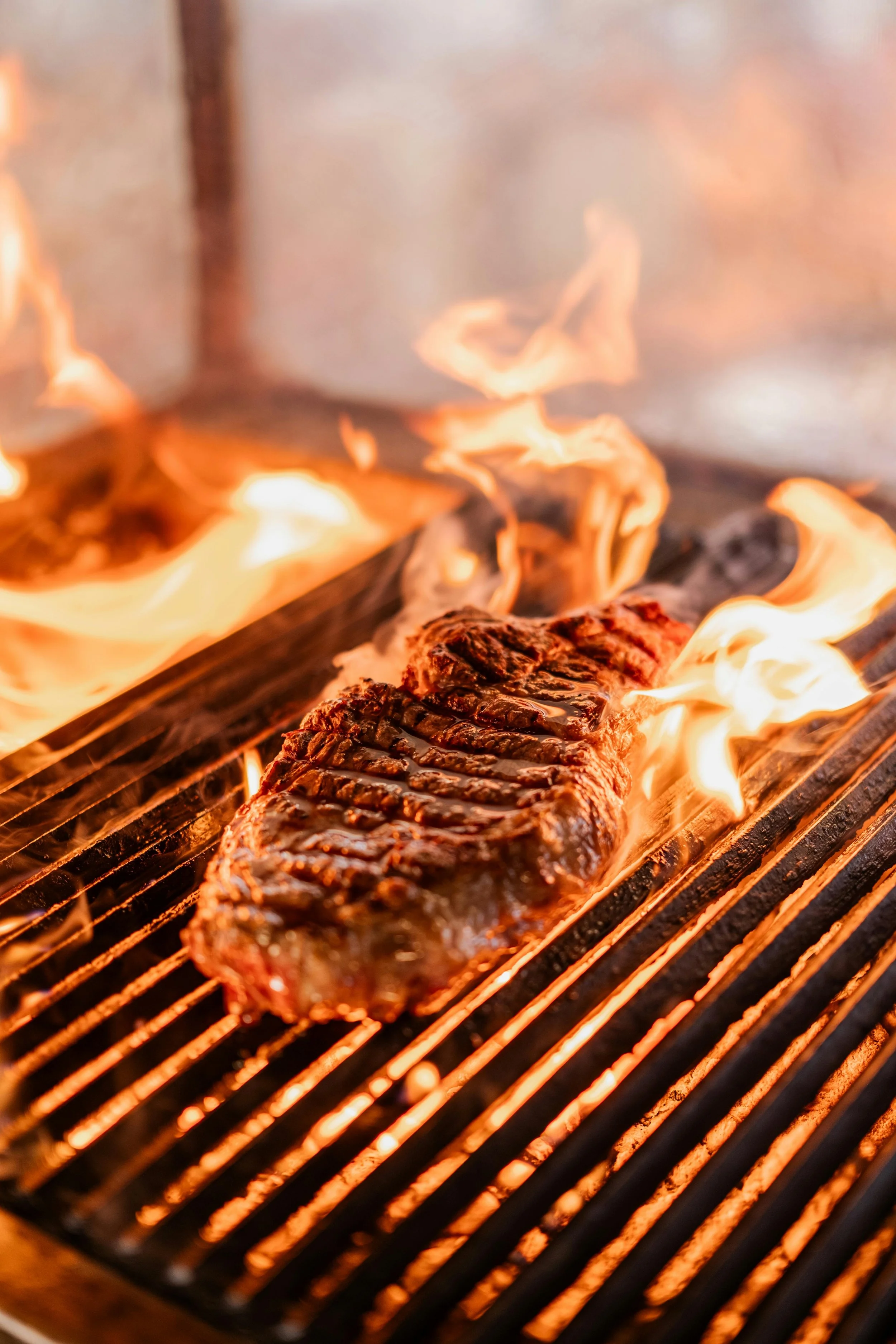A steak cooking on a grill with flames and heat coming from below.
