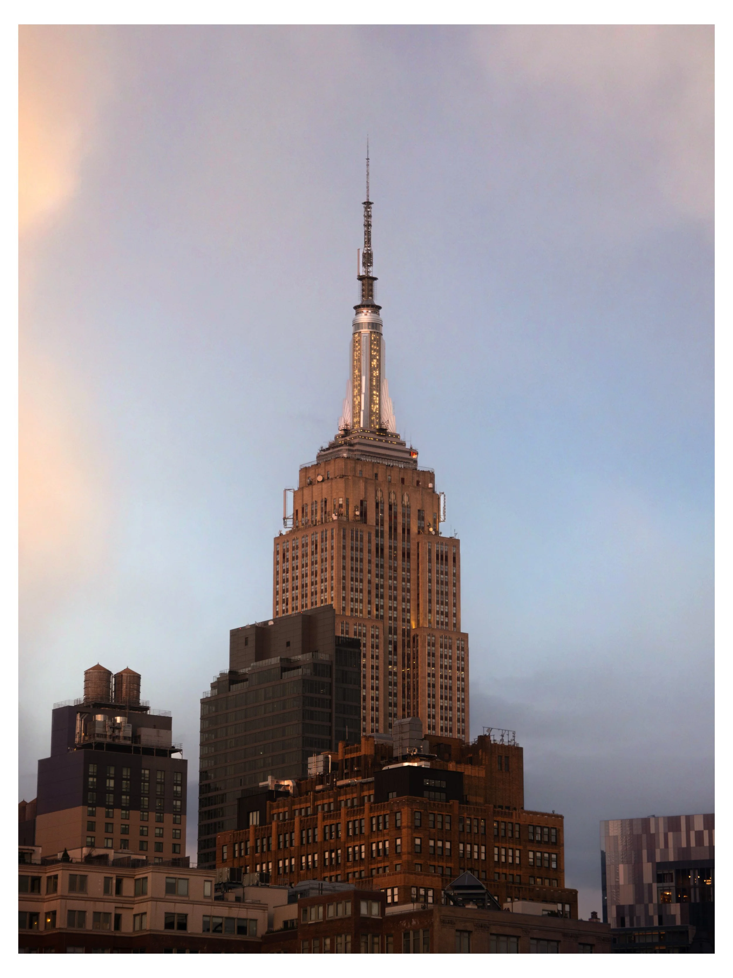 The Empire State Building in New York City during dusk, with neighboring skyscrapers and an overcast sky.