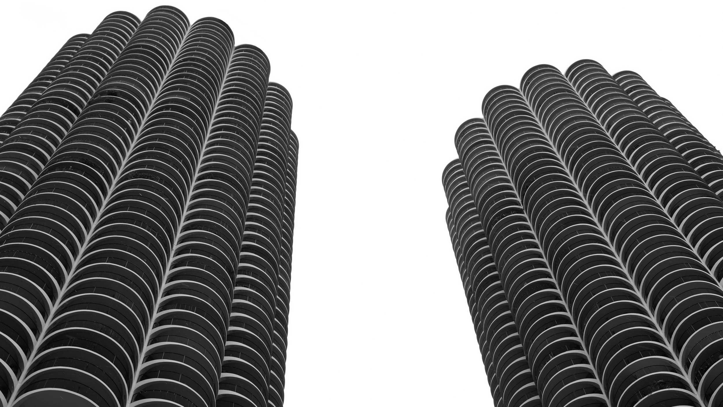 Low-angle view of two tall, cylindrical buildings with numerous rounded balconies, set against a white sky.
