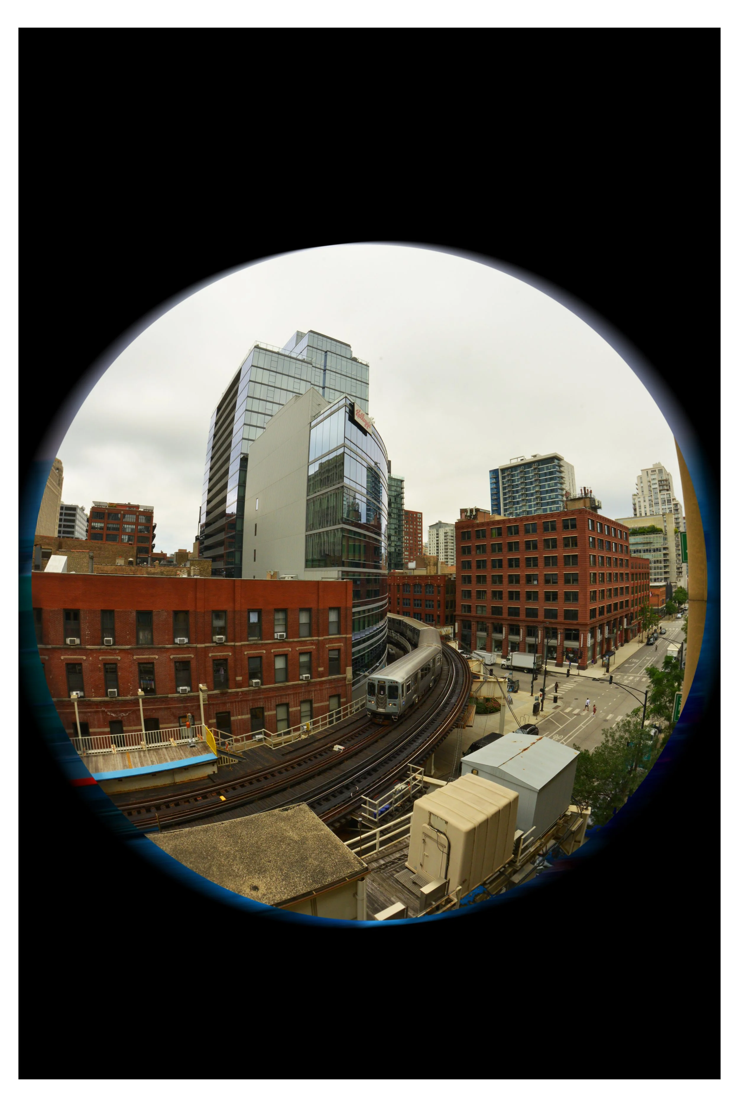 View of city buildings, railroad track with a train, and streets below, seen through a rounded window or opening.
