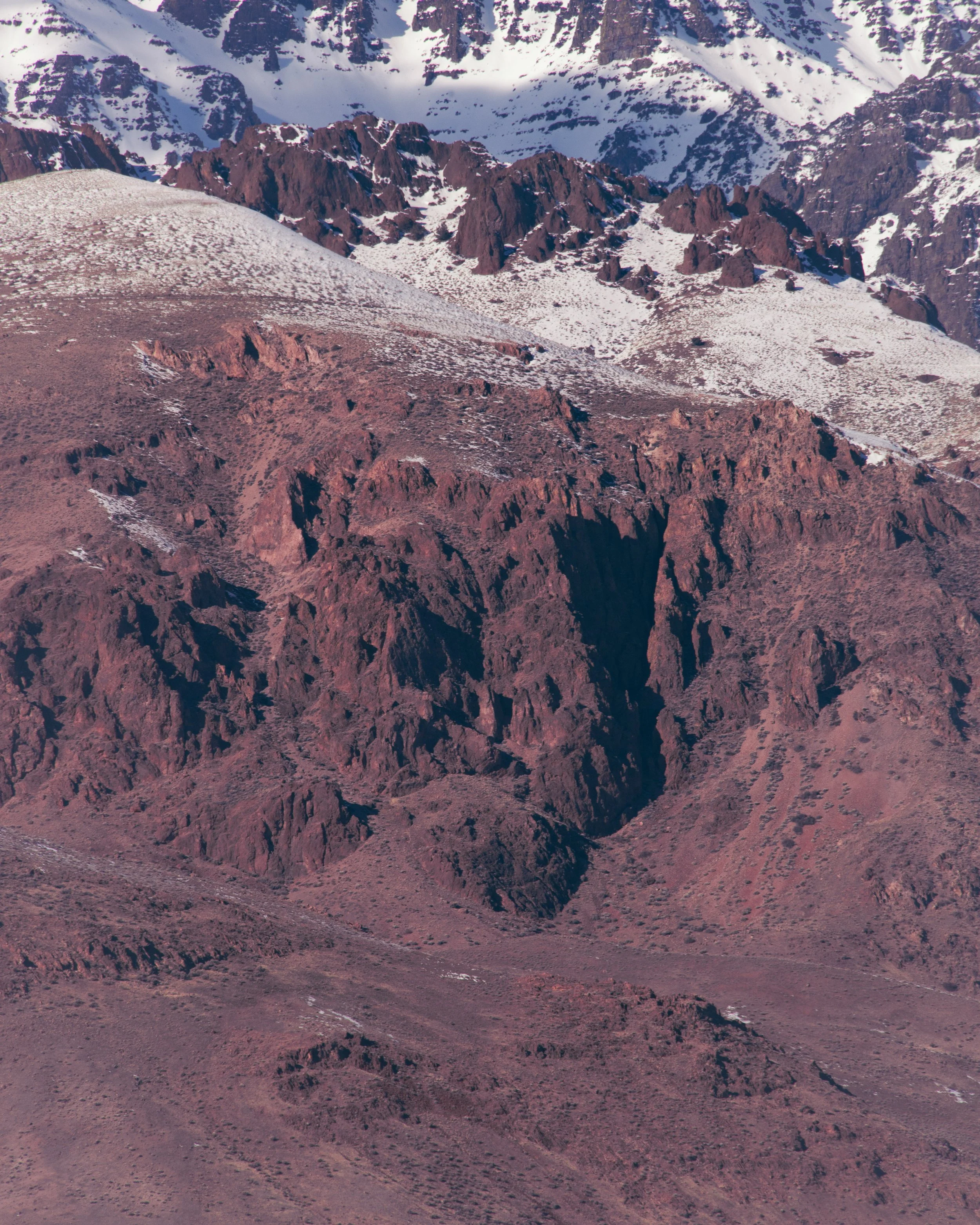 Mountain landscape with snow-capped peaks and reddish-brown rocky slopes.
