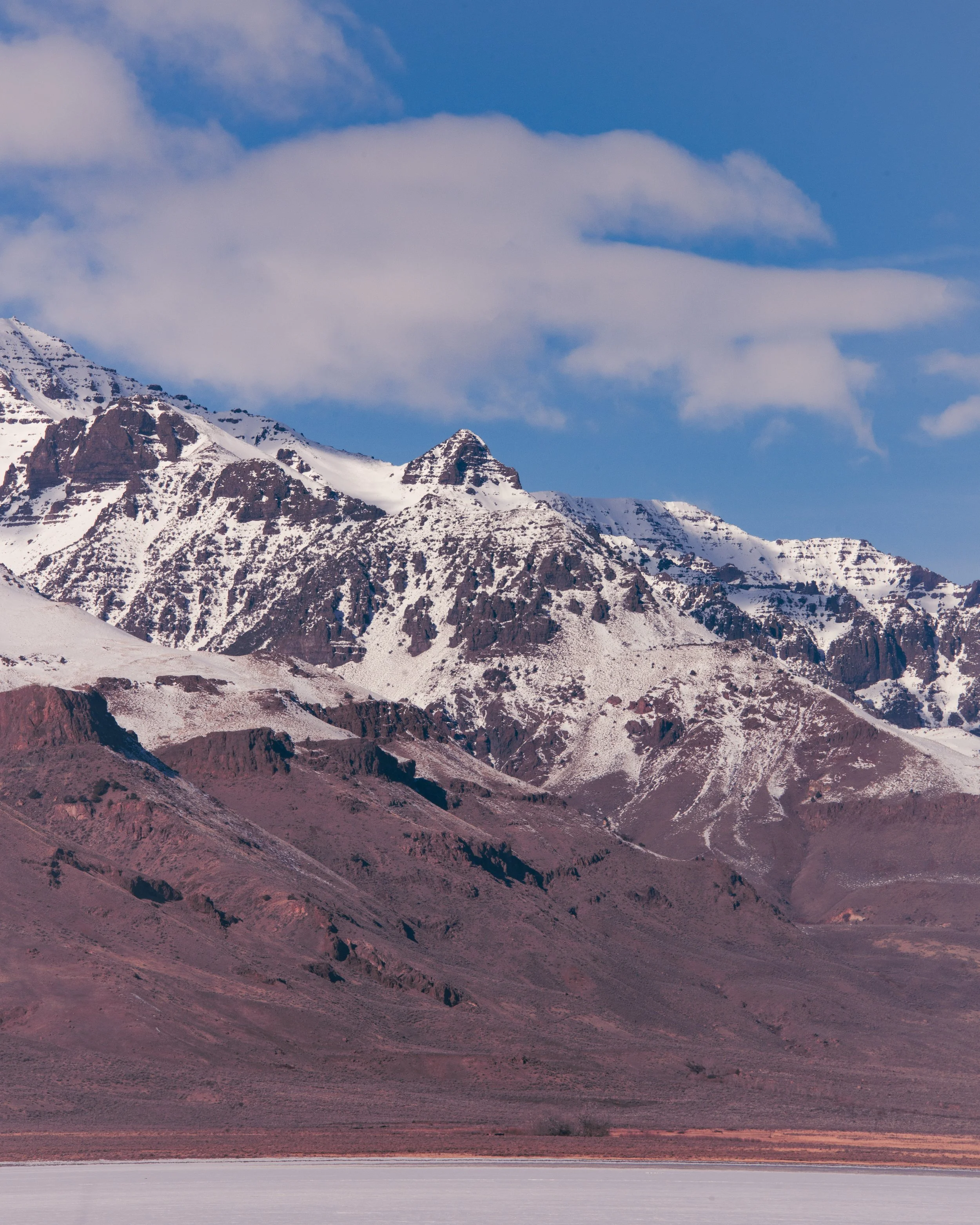 Snow-covered mountain range with rugged peaks under a blue sky with scattered clouds.