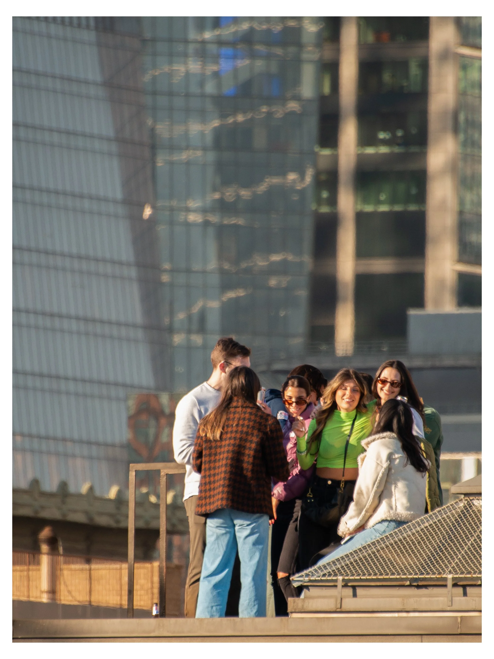 A group of seven young adults standing together outdoors, smiling and talking, with a modern building with reflective glass windows in the background.