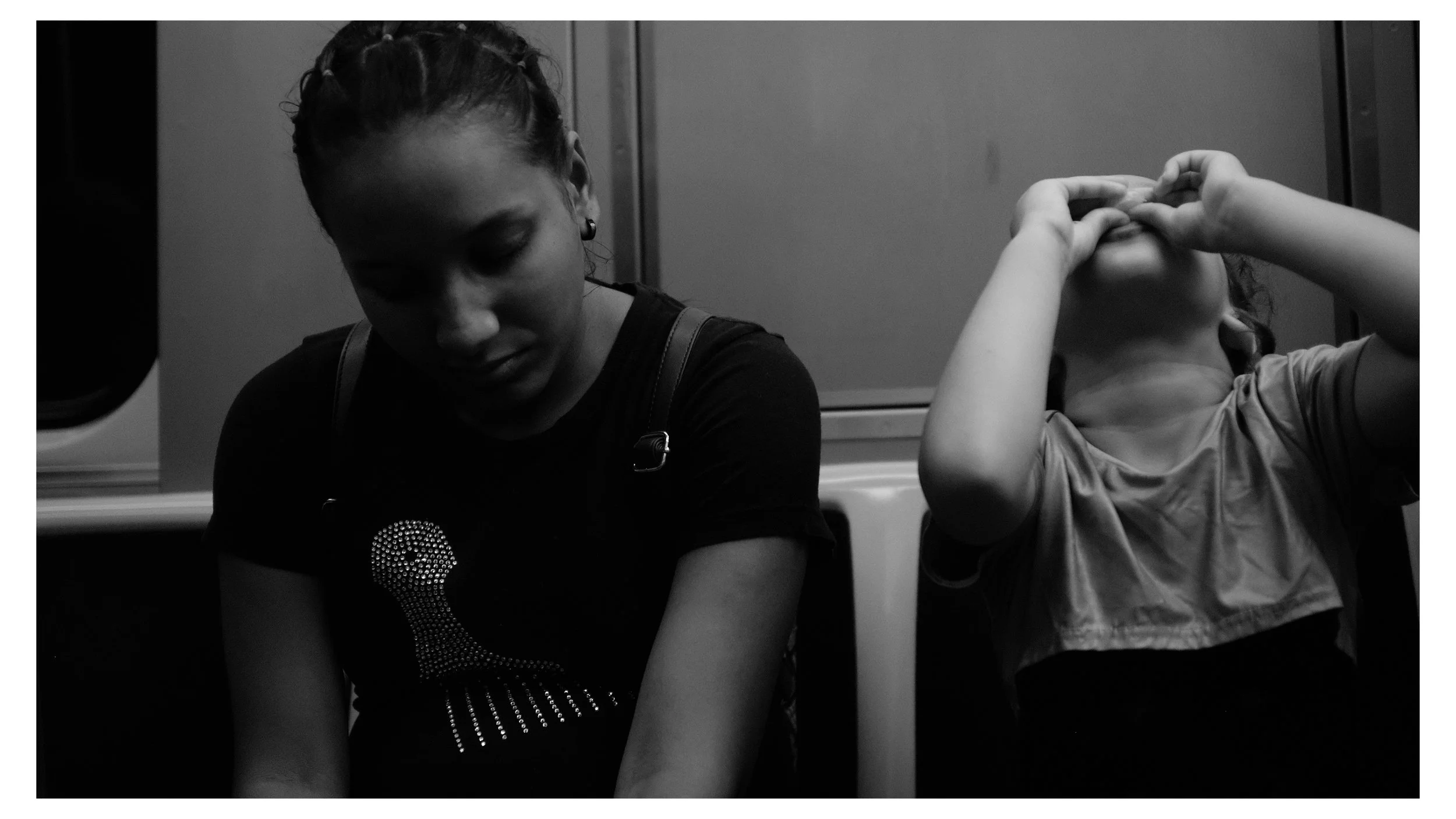 A woman and a young girl sitting on a train, both with their heads bowed or hands covering their faces.