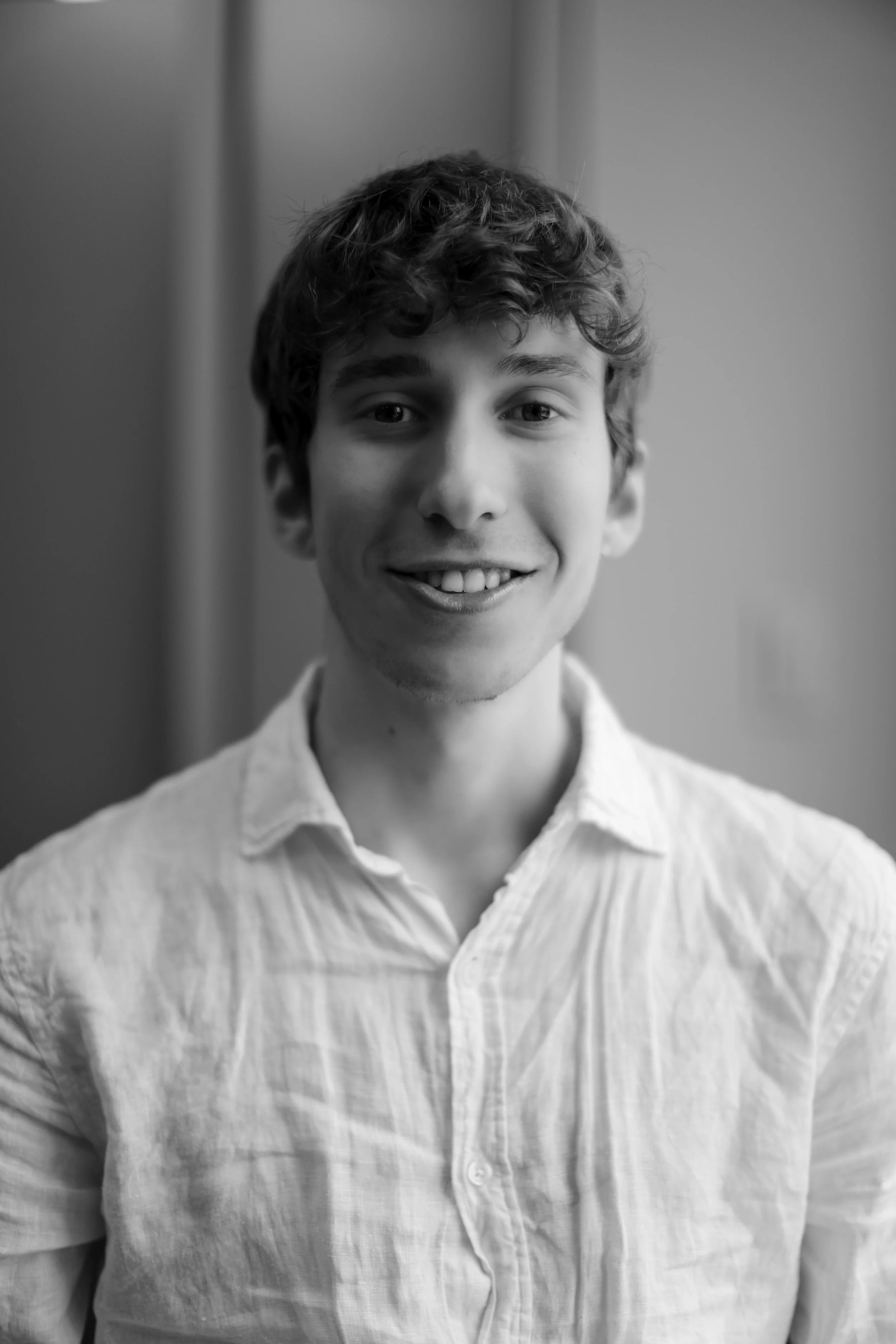 Close-up black and white photo of a young man with curly hair and a friendly smile, wearing a light-colored collared shirt.