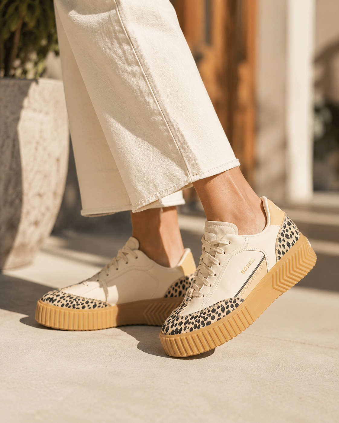 Women's casual sneakers with leopard-print accents worn with light pants.