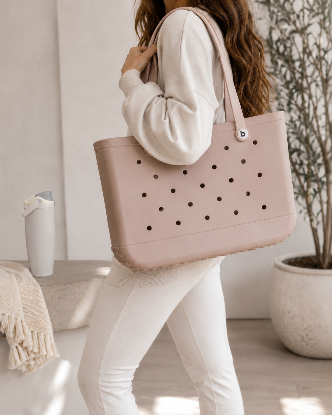 Woman carrying a large neutral tote bag with a water bottle.