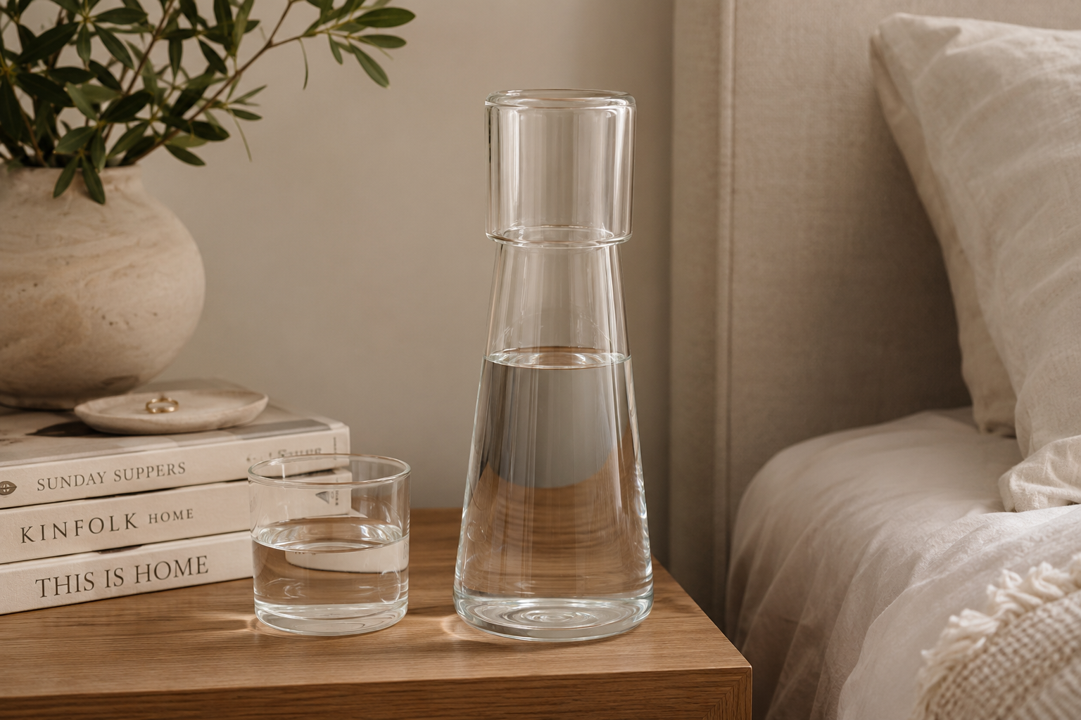 Glass bedside water carafe and drinking glass on a wooden nightstand.