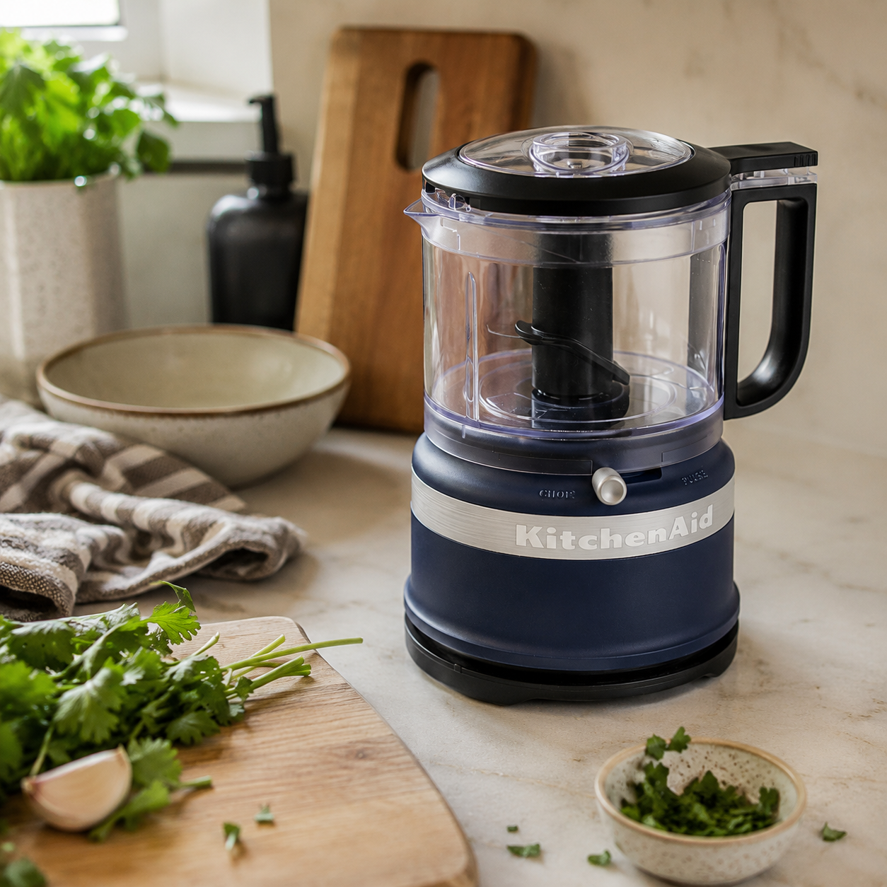 KitchenAid mini food processor on a kitchen counter with fresh herbs.