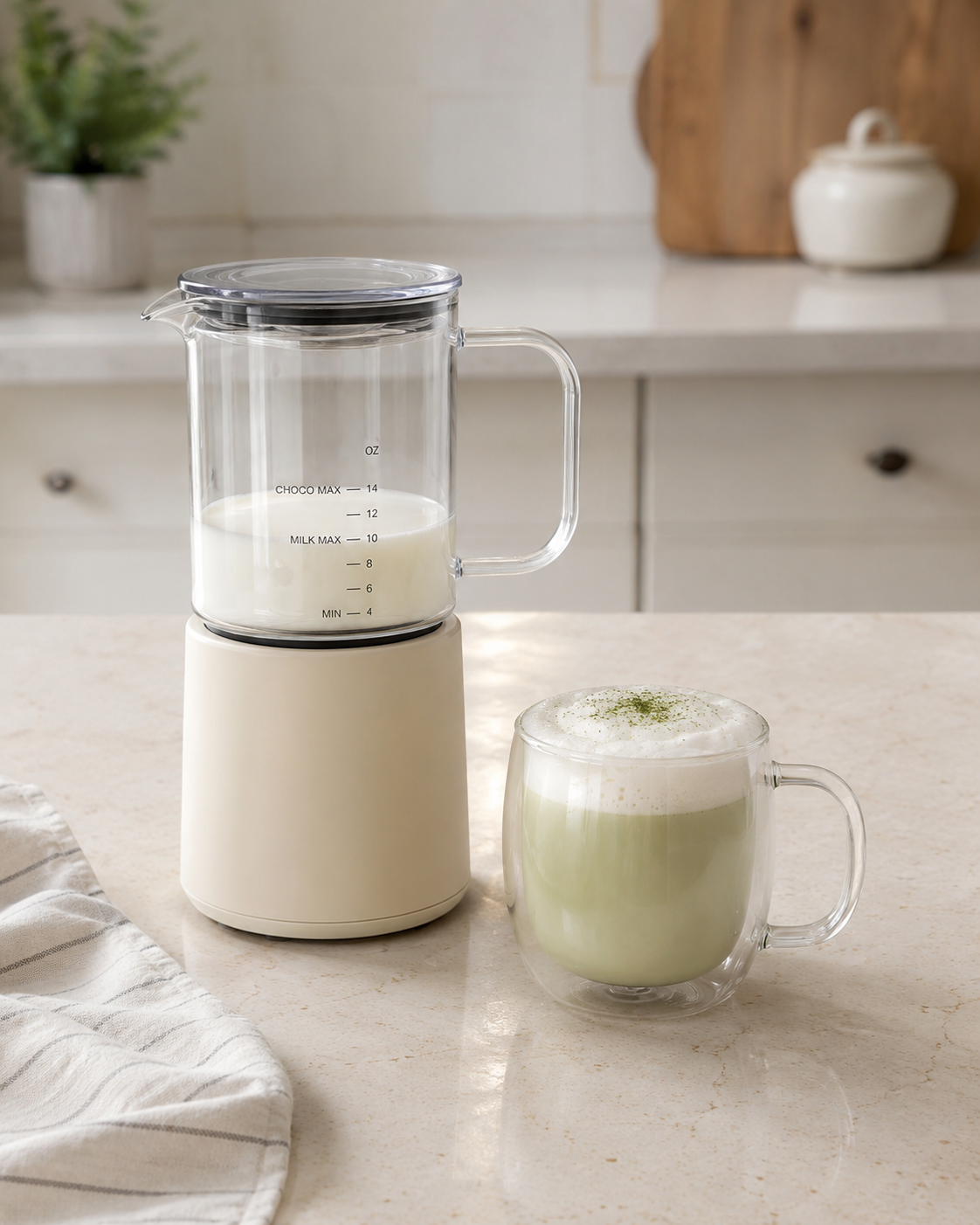Countertop milk frother and steamer beside a frothy green drink.