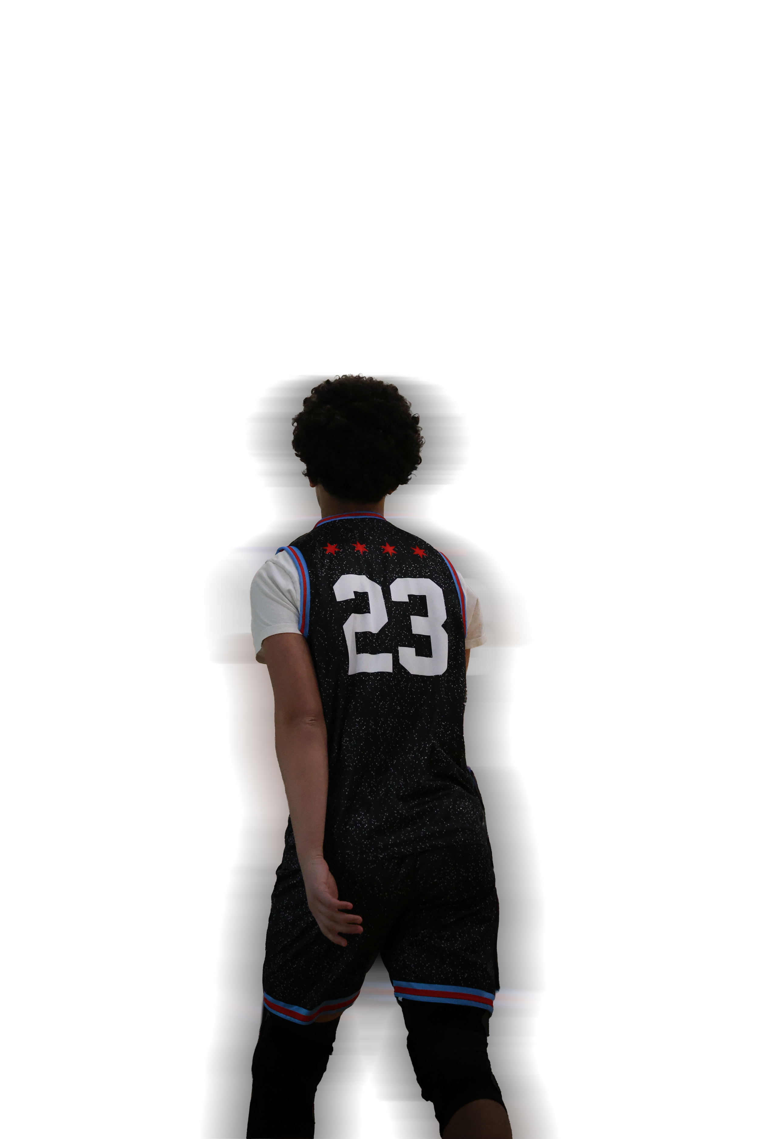 Back view of a young boy with curly hair, wearing a basketball jersey numbered 23, standing against a plain white background.