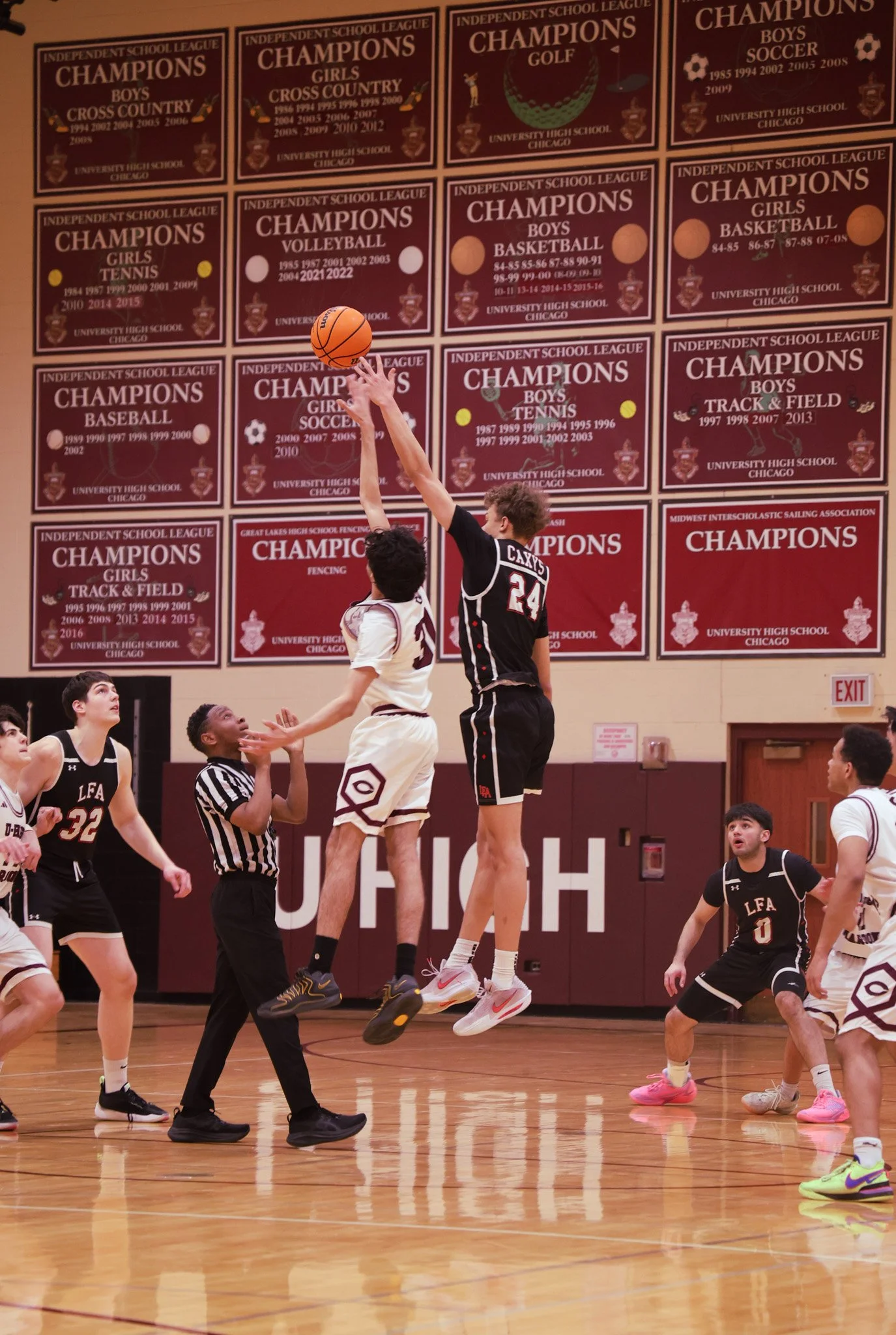 High school basketball game in a gymnasium with players jumping for a rebound, referees, and banners on the wall indicating championship victories.