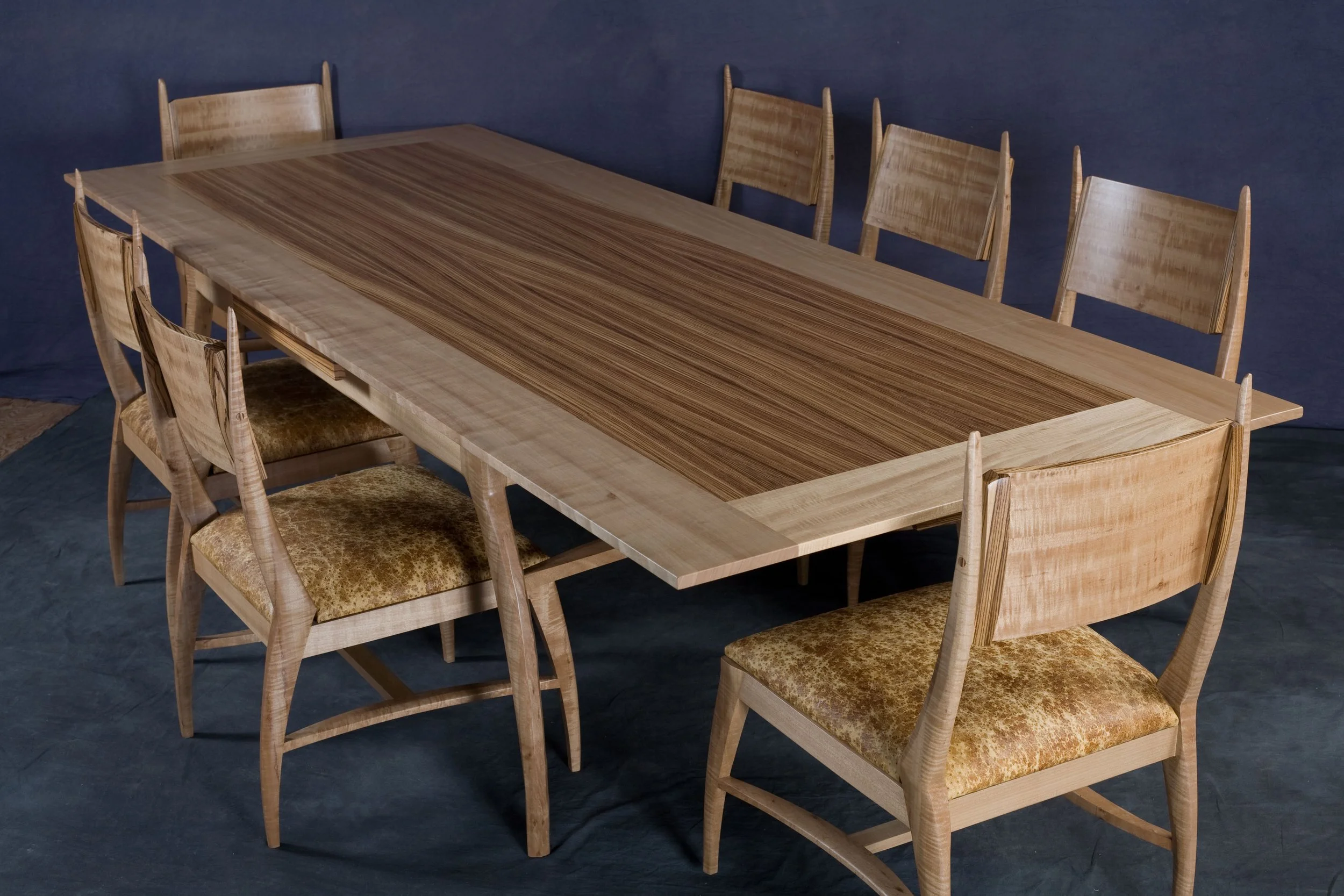 A wooden dining table with a striped wood surface, surrounded by eight matching wooden chairs with upholstered seats, set against a dark background.