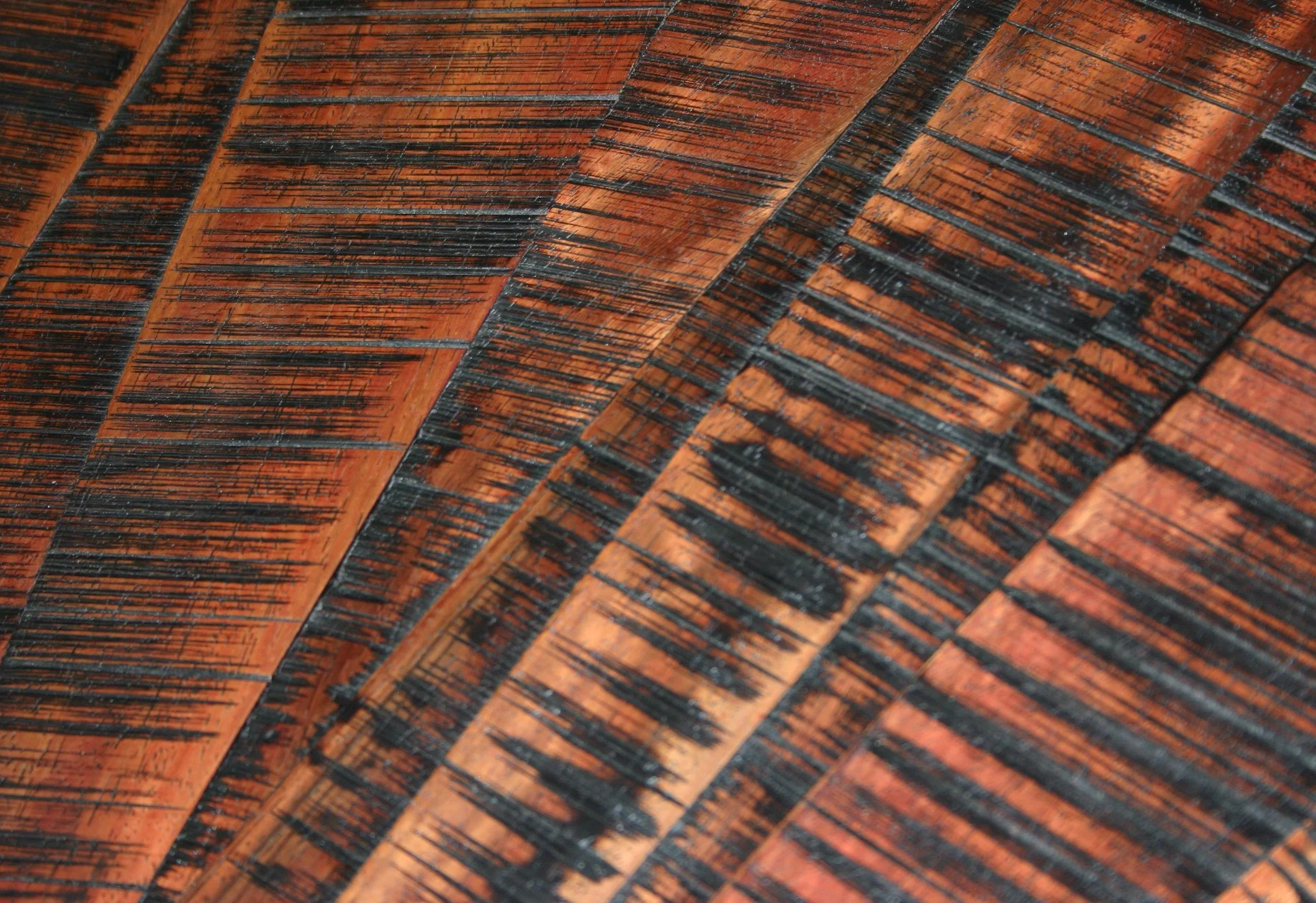 Close-up of a carved and stained wooden surface with detailed black burn marks and a reddish-brown hue.