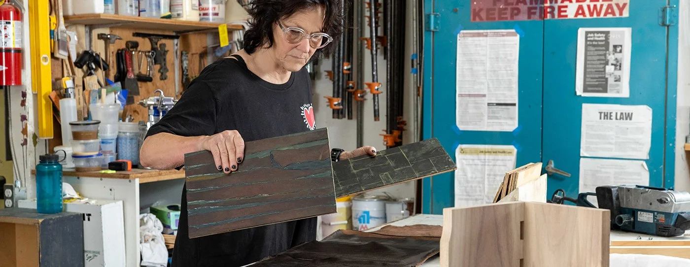 Collette in her workshop examining wooden planks and tiles with a focused expression.