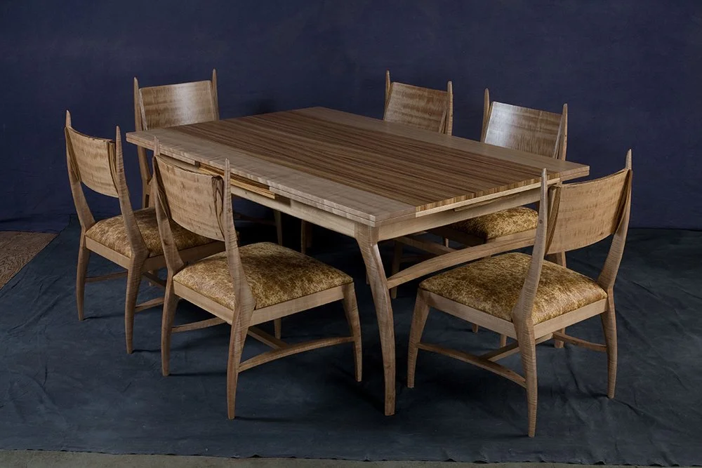 Wood dining table with six matching chairs, some with cushioned seats, on a dark fabric background.