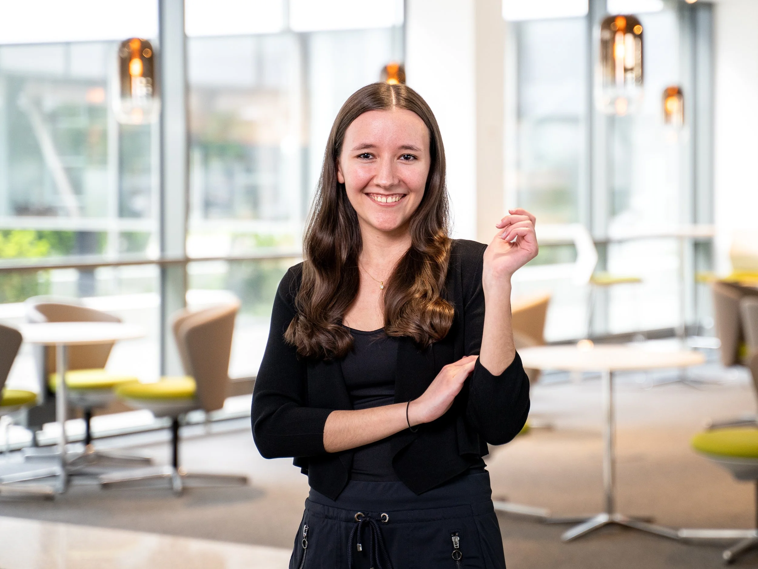 Teamfoto einer jungen Mitarbeiterin im modernen Unternehmenslounge-Bereich mit großer Glasfront – natürliche Business-Portraitfotografie für Karriereseiten und LinkedIn