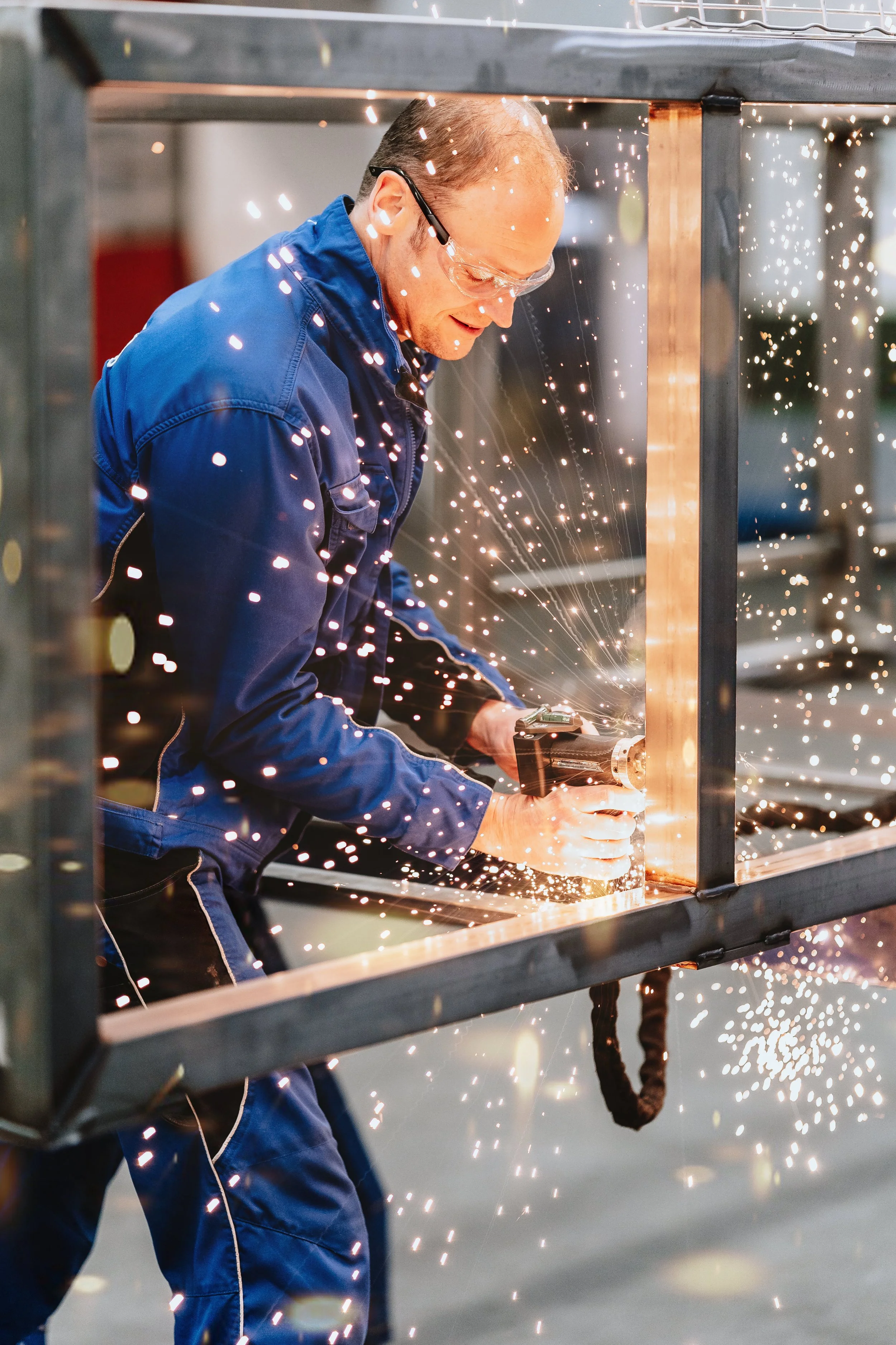 Detailaufnahme eines Schweißers mit Schutzhelm und grünen Handschuhen beim Präzisionsschweißen in der Maschinenfabrik – industrielle Corporate Fotografie Niklas Schulz