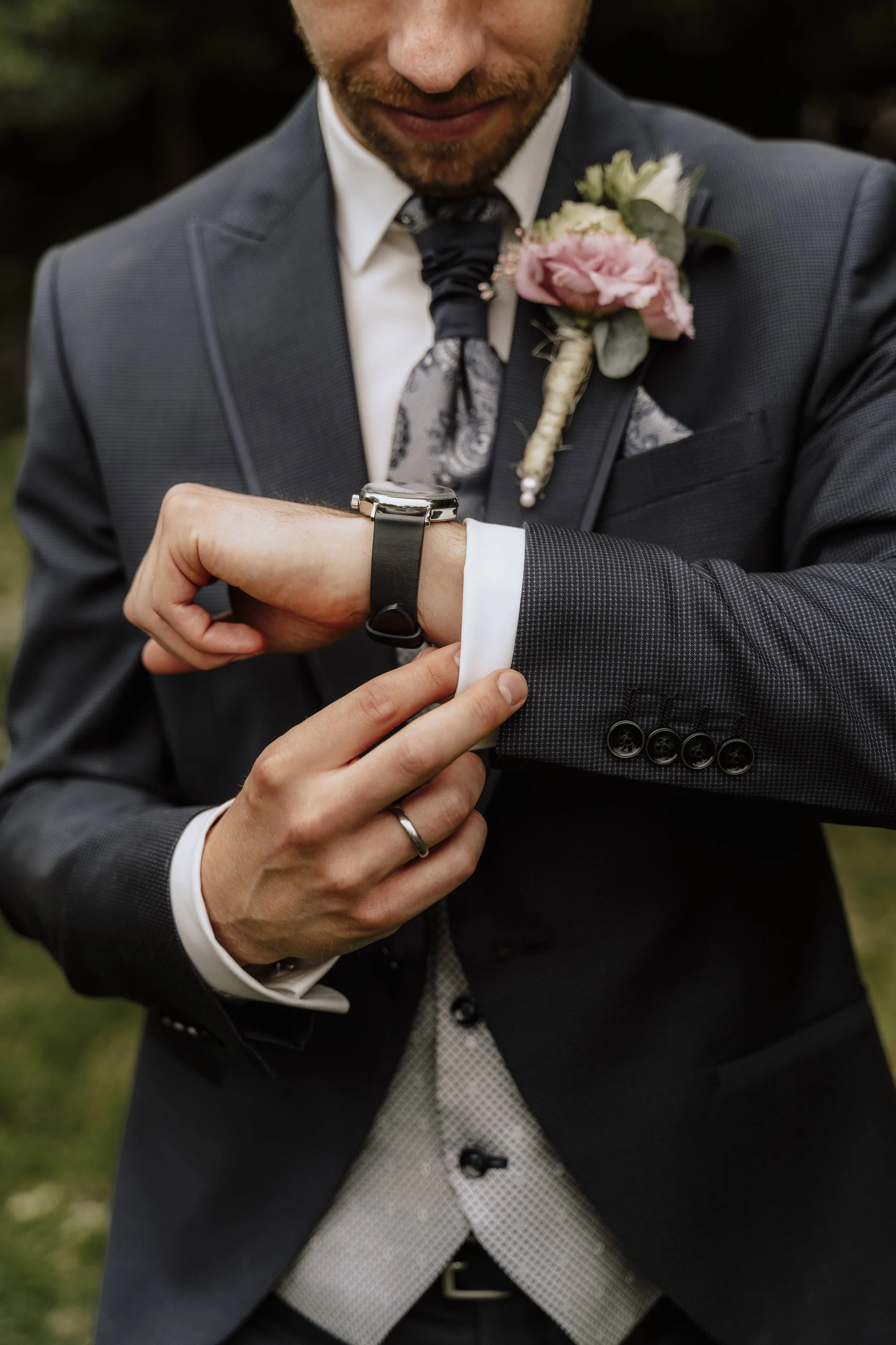 Bräutigam richtet seine Armbanduhr, Detailaufnahme mit rosa-weißer Ansteckblume – Hochzeitsfotograf Tierpark Sababurg
