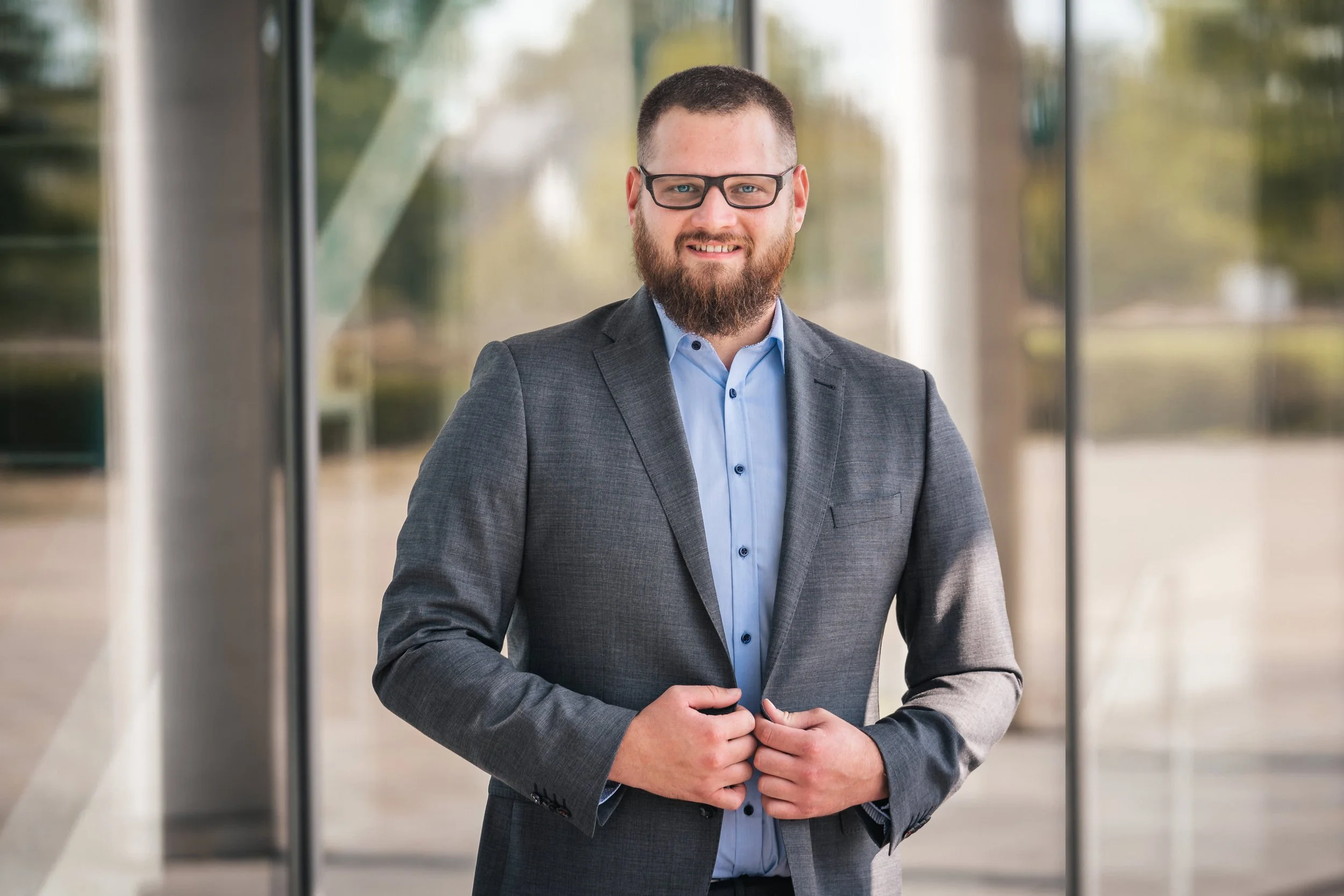 Professionelles Businessportrait eines Unternehmers im grauen Anzug vor Glasfassade – authentischer Headshot für LinkedIn und Unternehmenswebsite, Fotograf Niklas Schulz