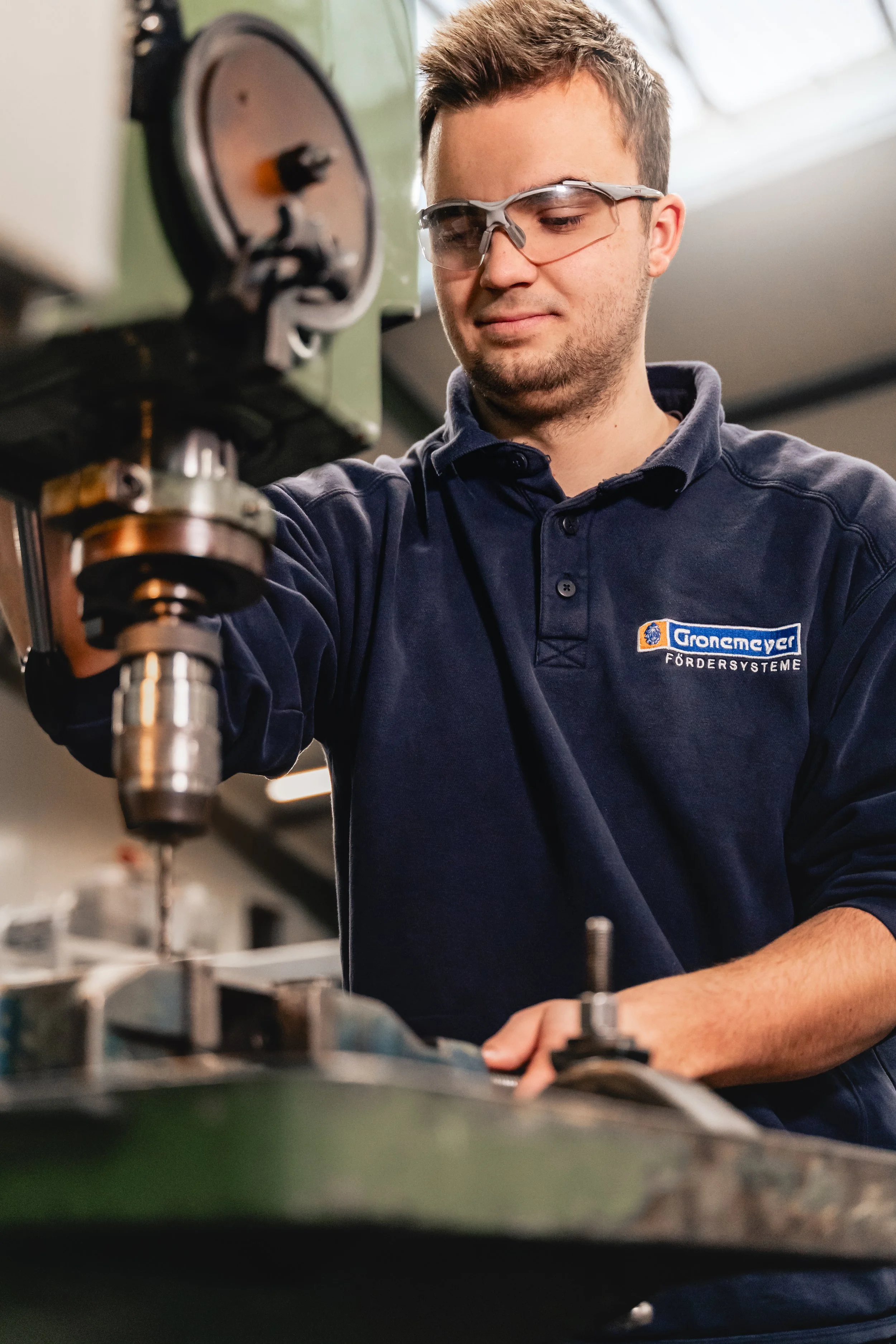 Auszubildender der Gronemeyer Fördersysteme arbeitet konzentriert an einer Bohrmaschine mit Schutzbrille – Unternehmensreportage Ausbildung und Employer Branding OWL