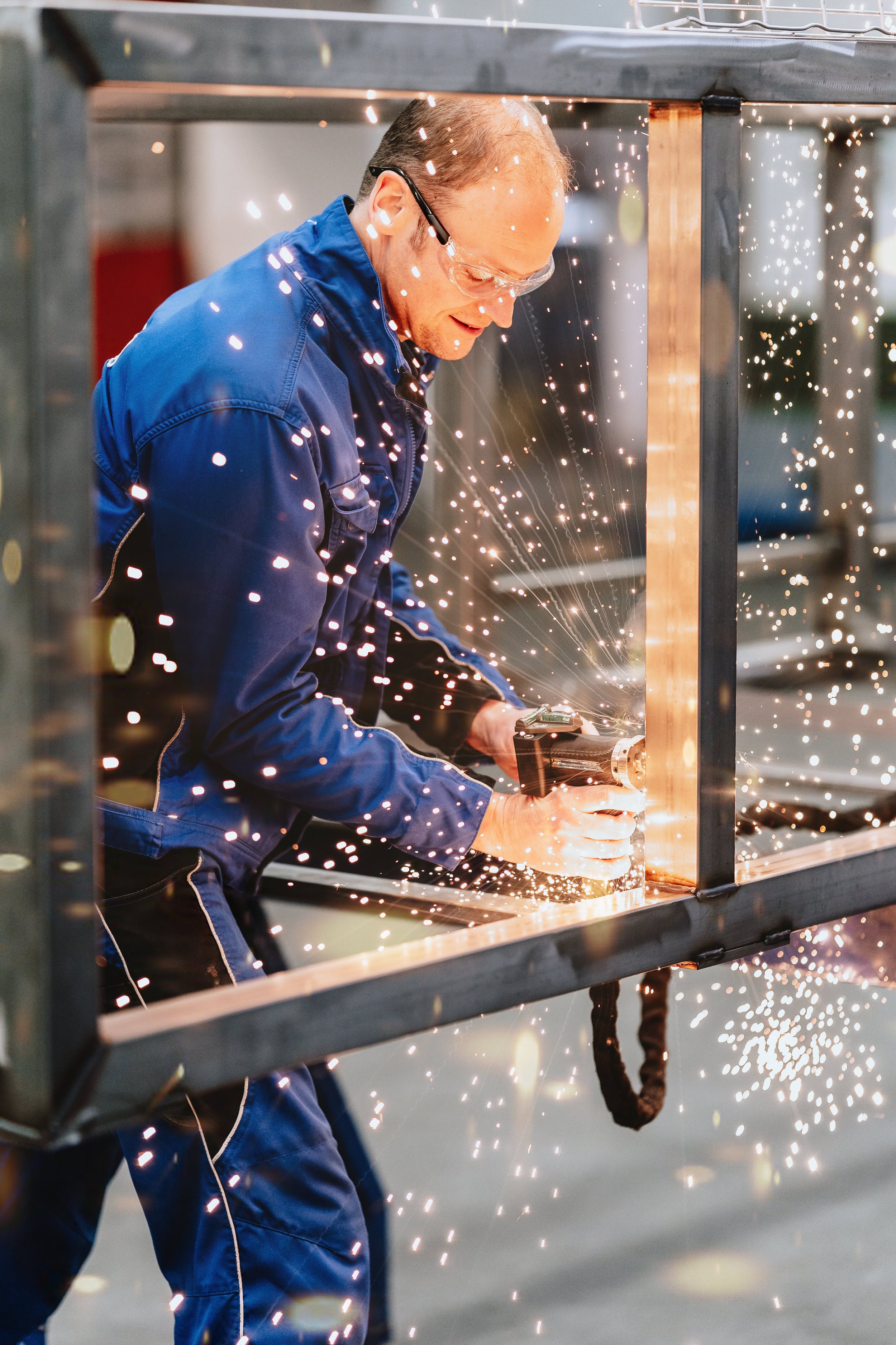 Ein Mann in Arbeitshandschuhen und Schutzbrille schweißt Metall, dabei sprühen Funken um ihn herum.
