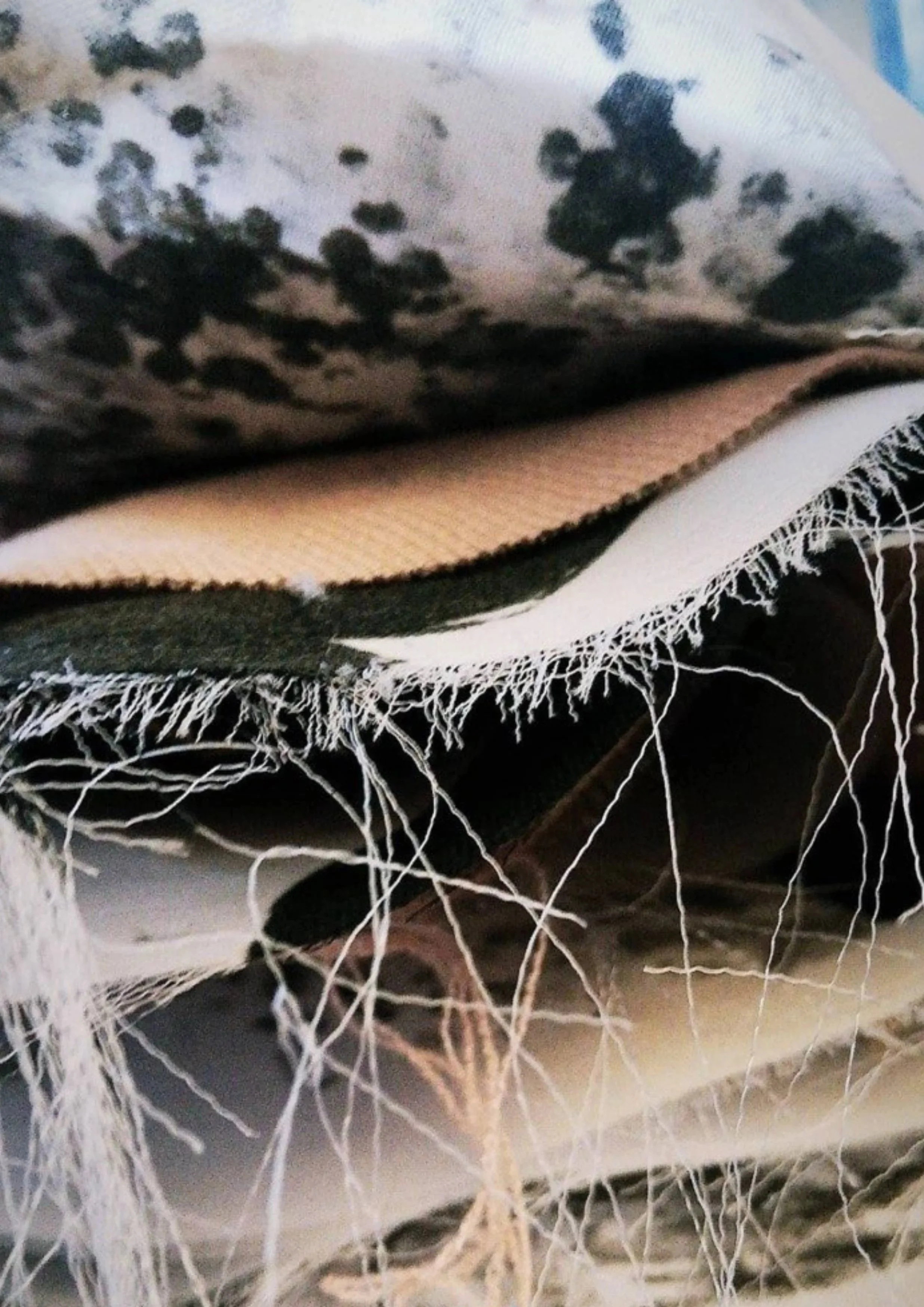 Close-up of a black and white Dalmatian puppy with distinctive spots resting on a textured blanket with dangling threads.